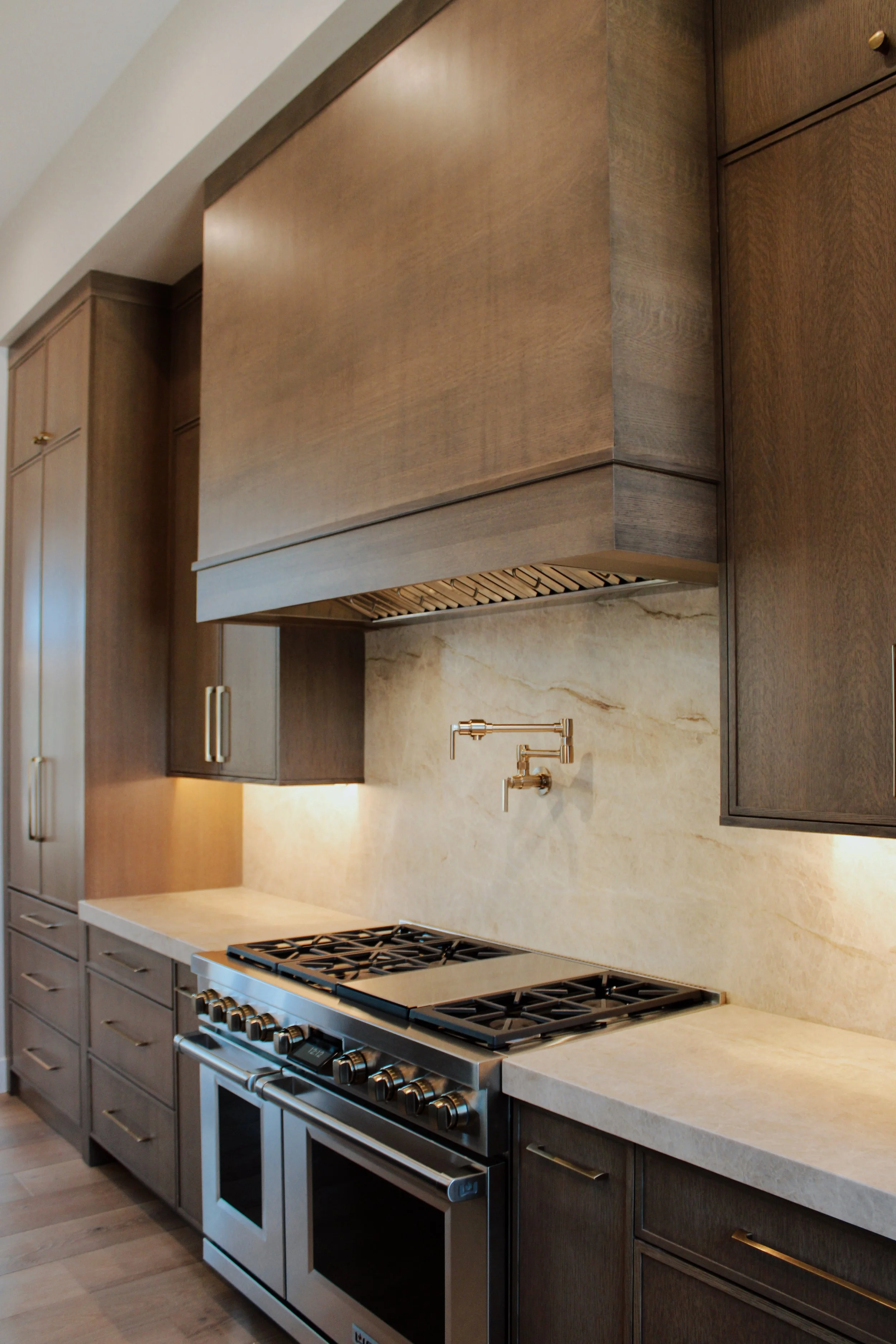 Modern kitchen with dark wood cabinets, beige marble backsplash, and a stainless steel stove with six burners.