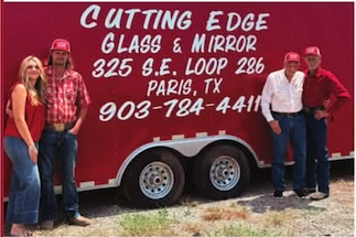 Four people standing in front of a red trailer with white text advertising a glass and mirror business in Paris, Texas.