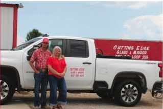 Two people standing in front of a white pickup truck with red and black branding for a glazing and mirror company.