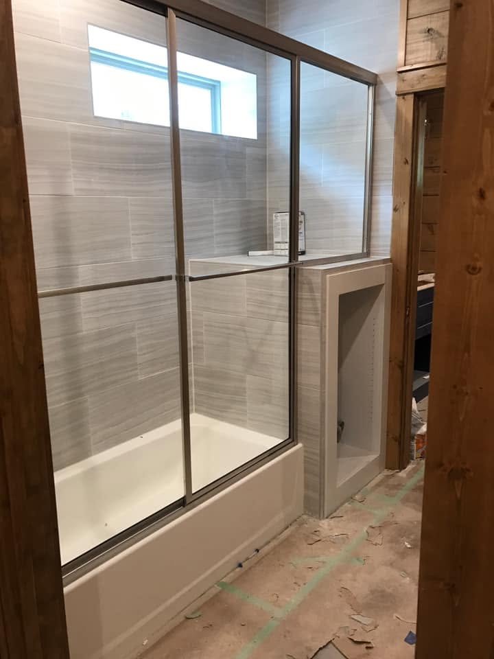 Glass shower enclosure installed above a bathtub, featuring clear glass panels and metal framing.