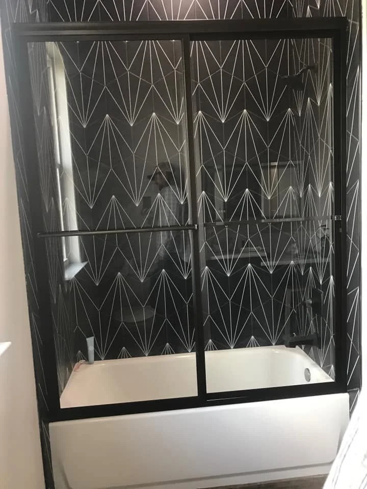 Black-framed sliding glass shower enclosure installed over a bathtub with patterned glass panels.