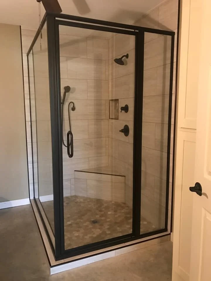 A modern glass shower enclosure with black metal framing, tiled walls, and a built-in bench inside a bathroom.