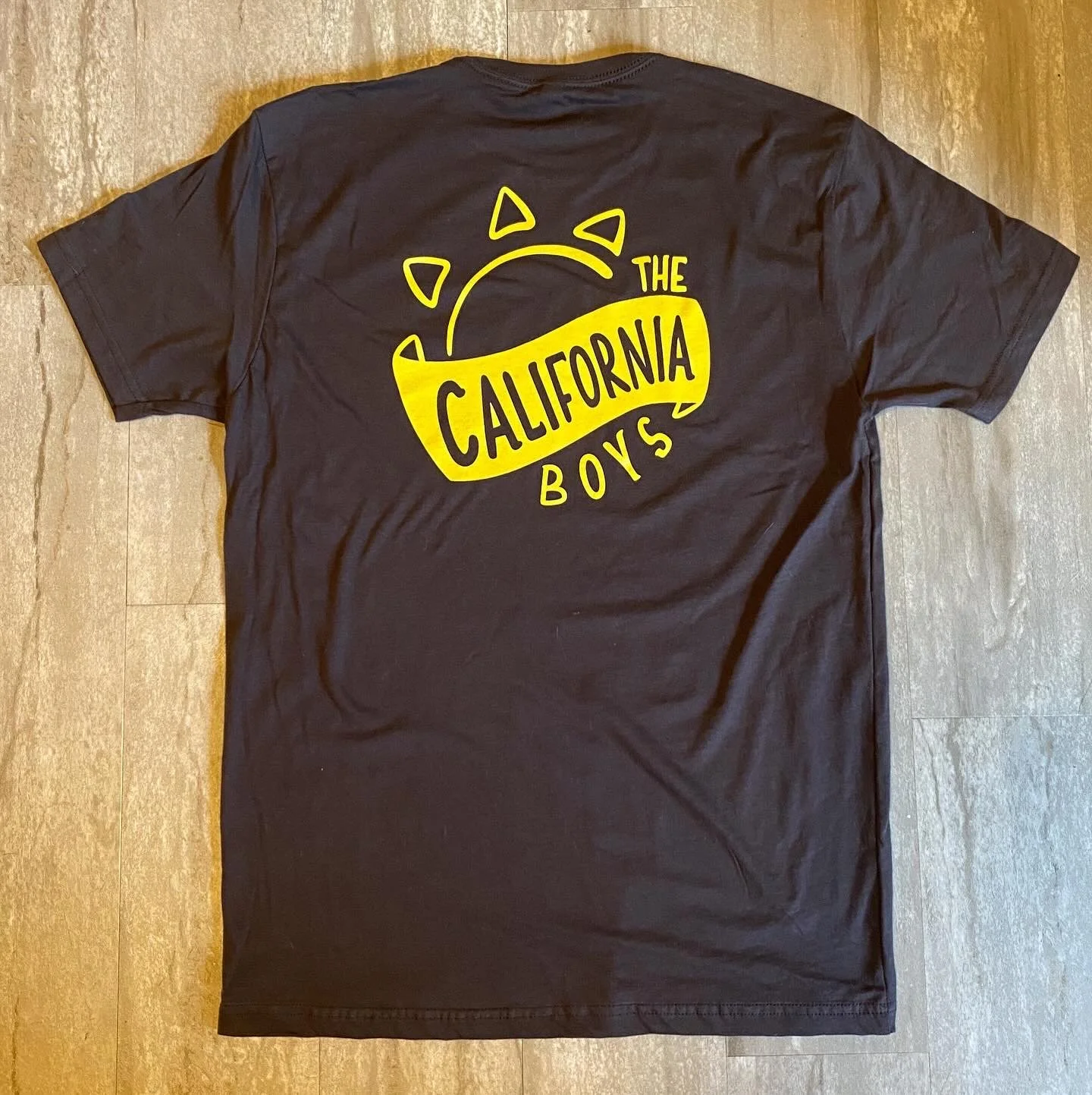 Back of a brown t-shirt with a yellow graphic of a sun and the text 'The California Boys'.