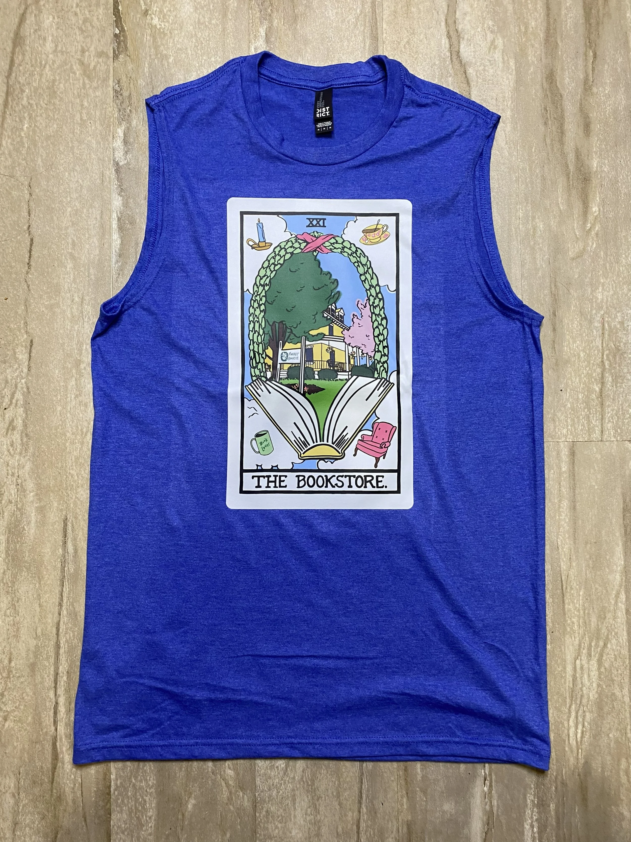Blue sleeveless T-shirt with a graphic inspired by a Tarot Card, which says "The Bookstore", featuring a tree, books, a house, and various objects.