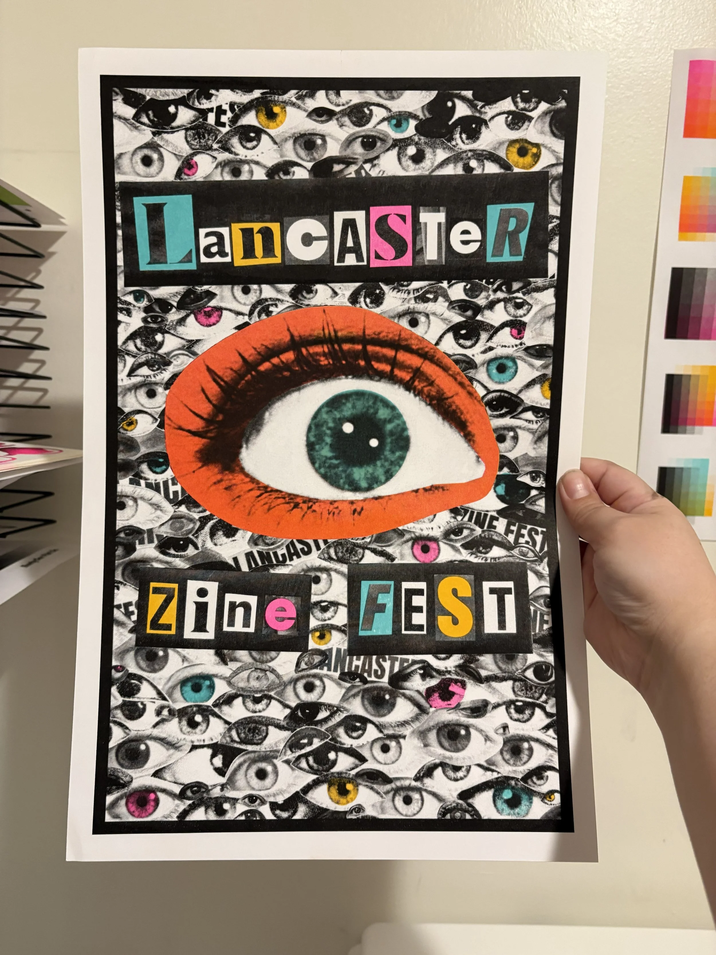 A poster with numerous black and white eye illustrations, with some colored eyes, featuring a large eye with an orange outline and green iris. The words 'Lancaster' and 'zine fest' are displayed in colorful, cut-out style letters.