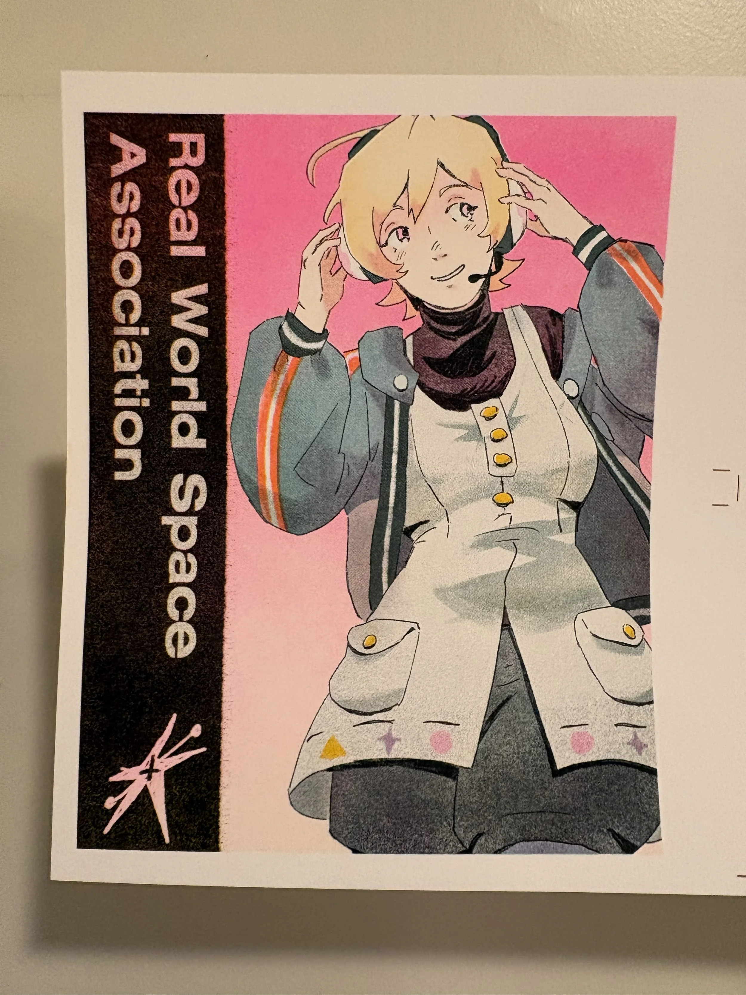 A risograph printed Anime-style drawing of a smiling blonde-haired person wearing a headset with a microphone, a gray jacket with orange stripes, a tartan and star patterned shirt, and beige shorts, against a pink background 