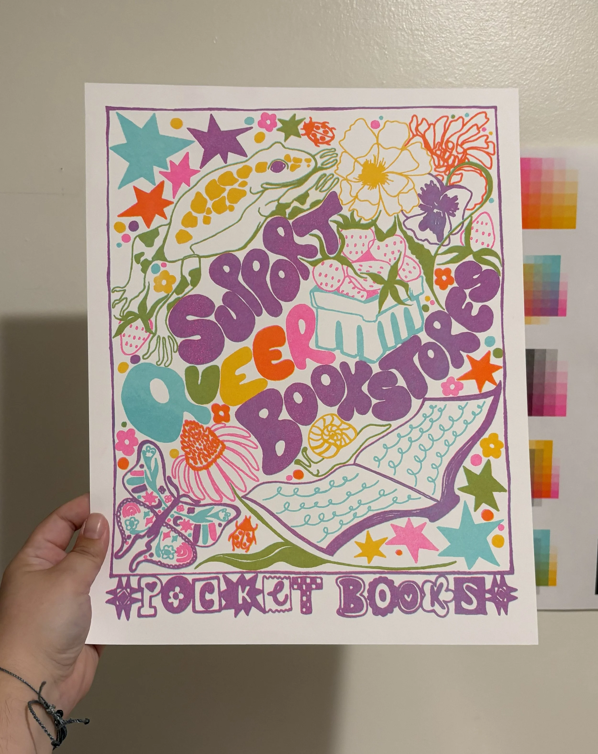 A risograph print of an illustration with the text "Support Queer Bookstores" surrounded by illustrations of a book, a frog, strawberries, stars, a butterfly, and more. The bottom says "Pocket Books". The print includes a rainbow of colors.