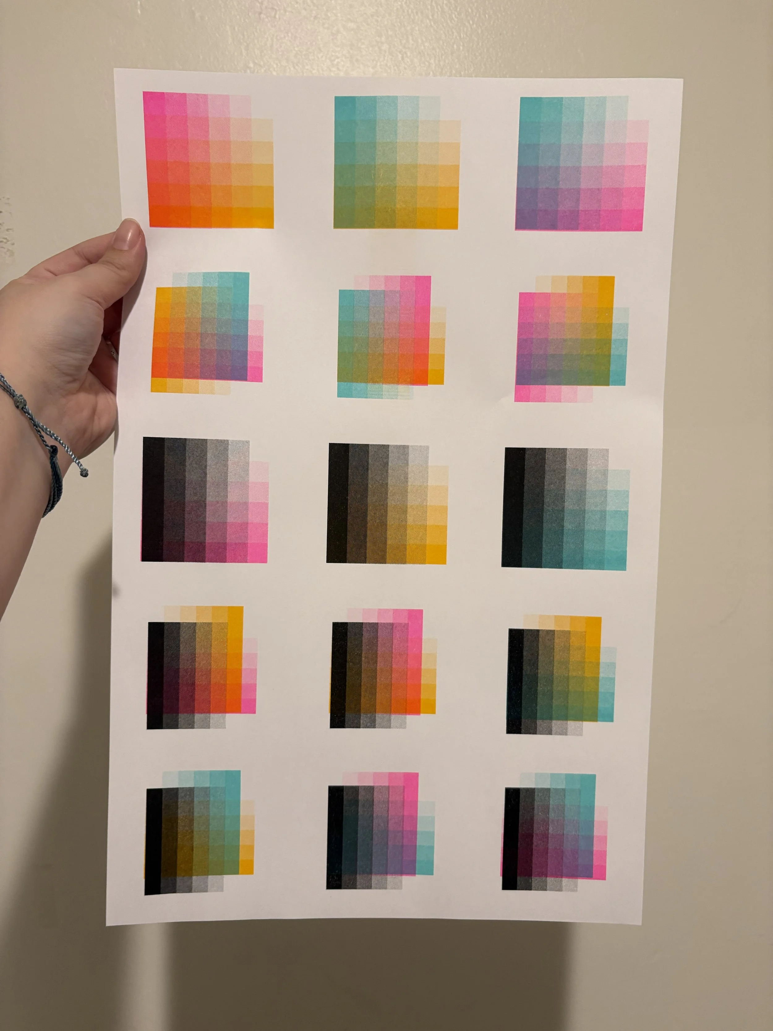 A person holding a sheet of risograph color test patches against a beige wall