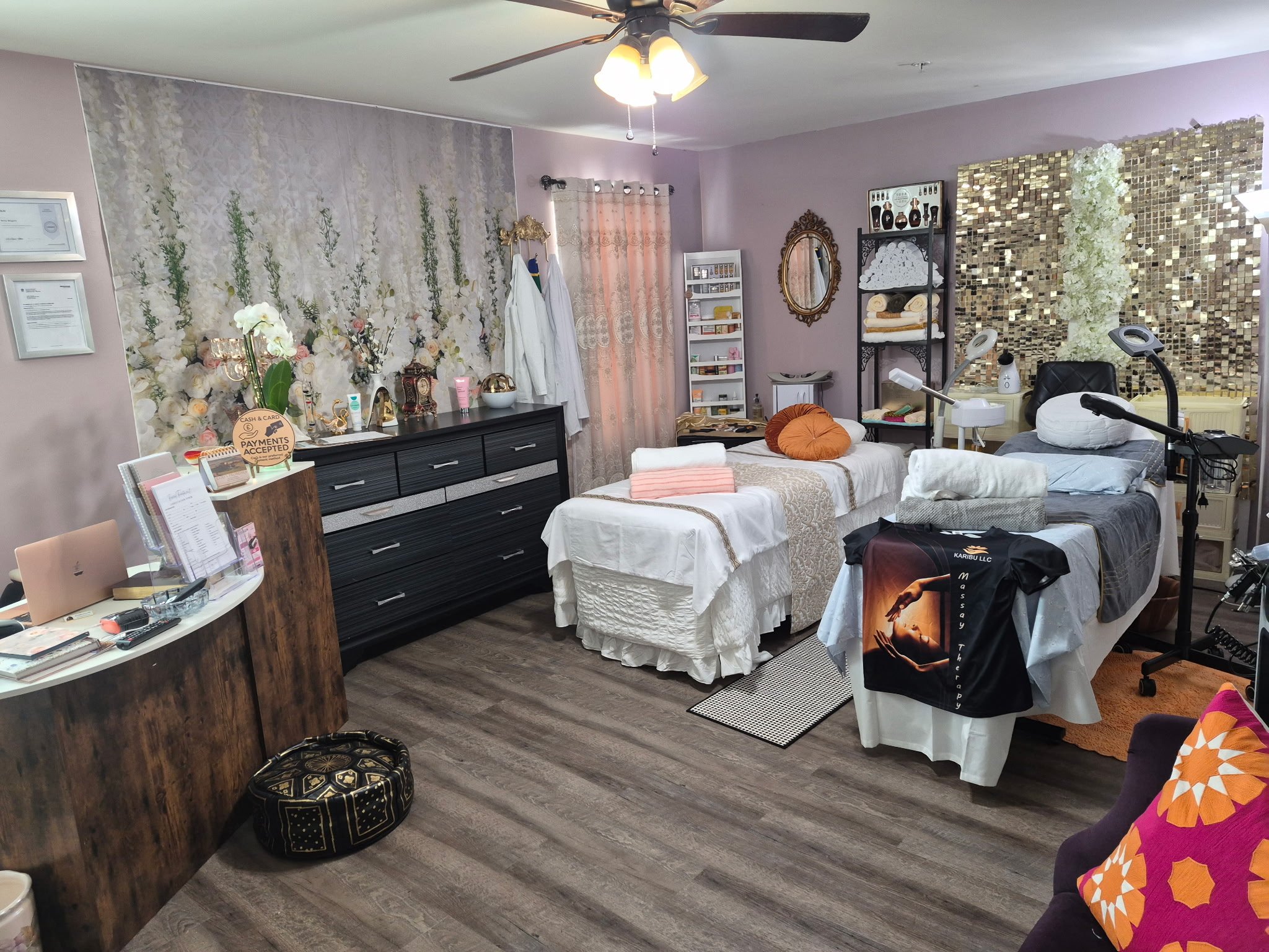 A room with purple walls decorated with various items including flowers, certificates, a mirror, shelves with towels and products, a chair with a pillow, and medical or therapy equipment.