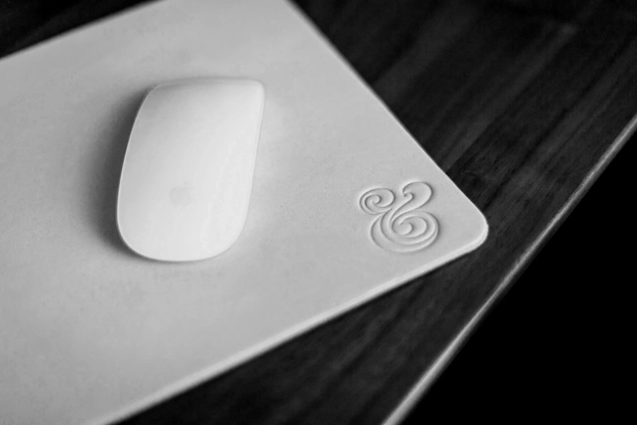 A white computer mouse sits on a mousepad with an ampersand embossed into it.
