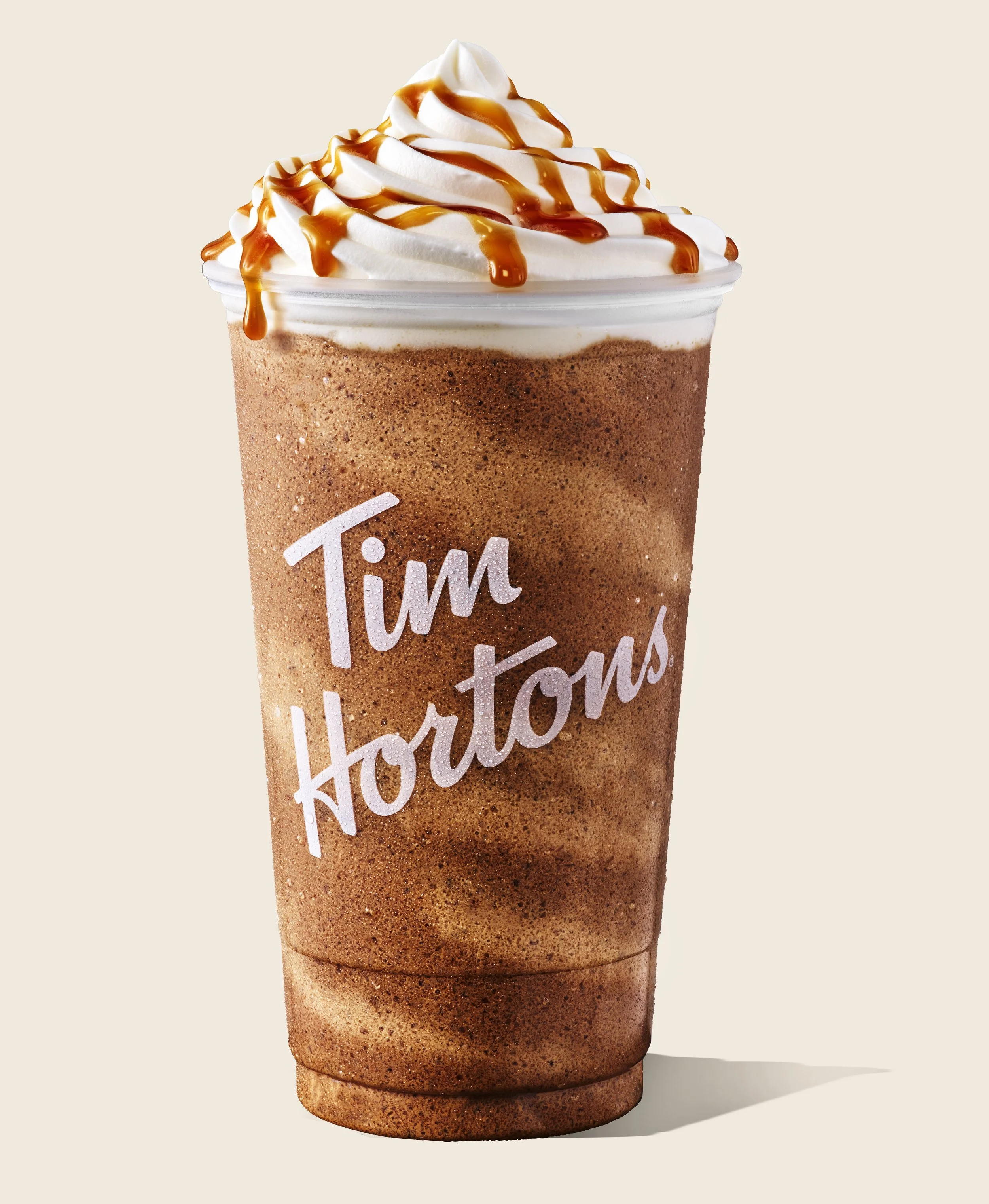 A Tim Hortons iced coffee topped with whipped cream and caramel drizzle in a clear plastic cup.