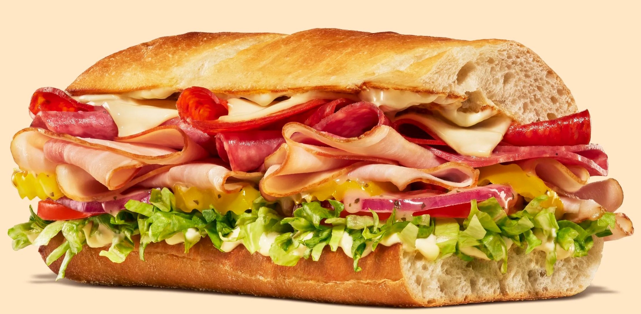 Sub sandwich with various deli meats, cheese, lettuce, tomato, and pickles on a baguette-style bread.