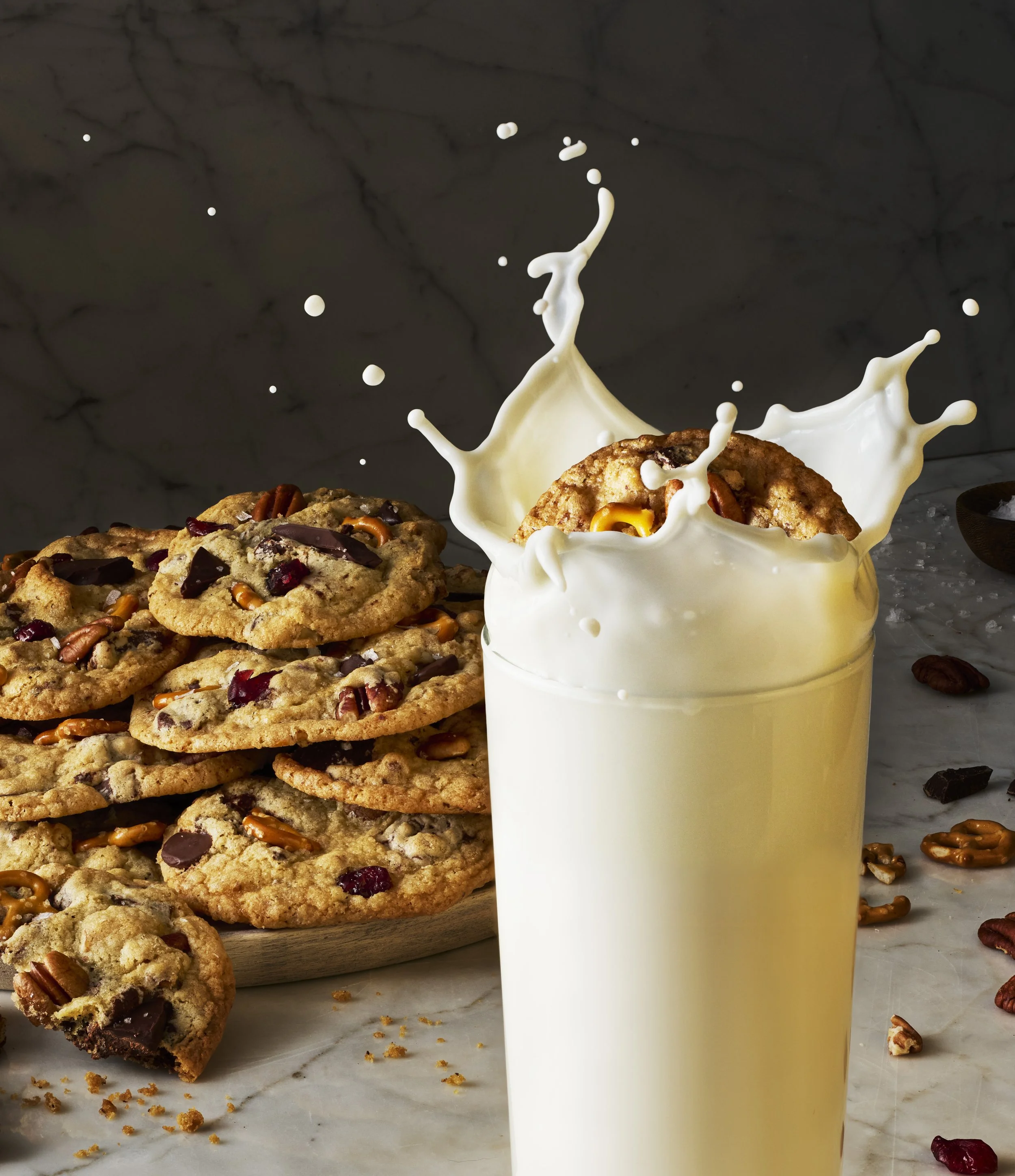 Chocolate chip cookies with pecans on a white marble surface and a glass of milk splashing with milk.