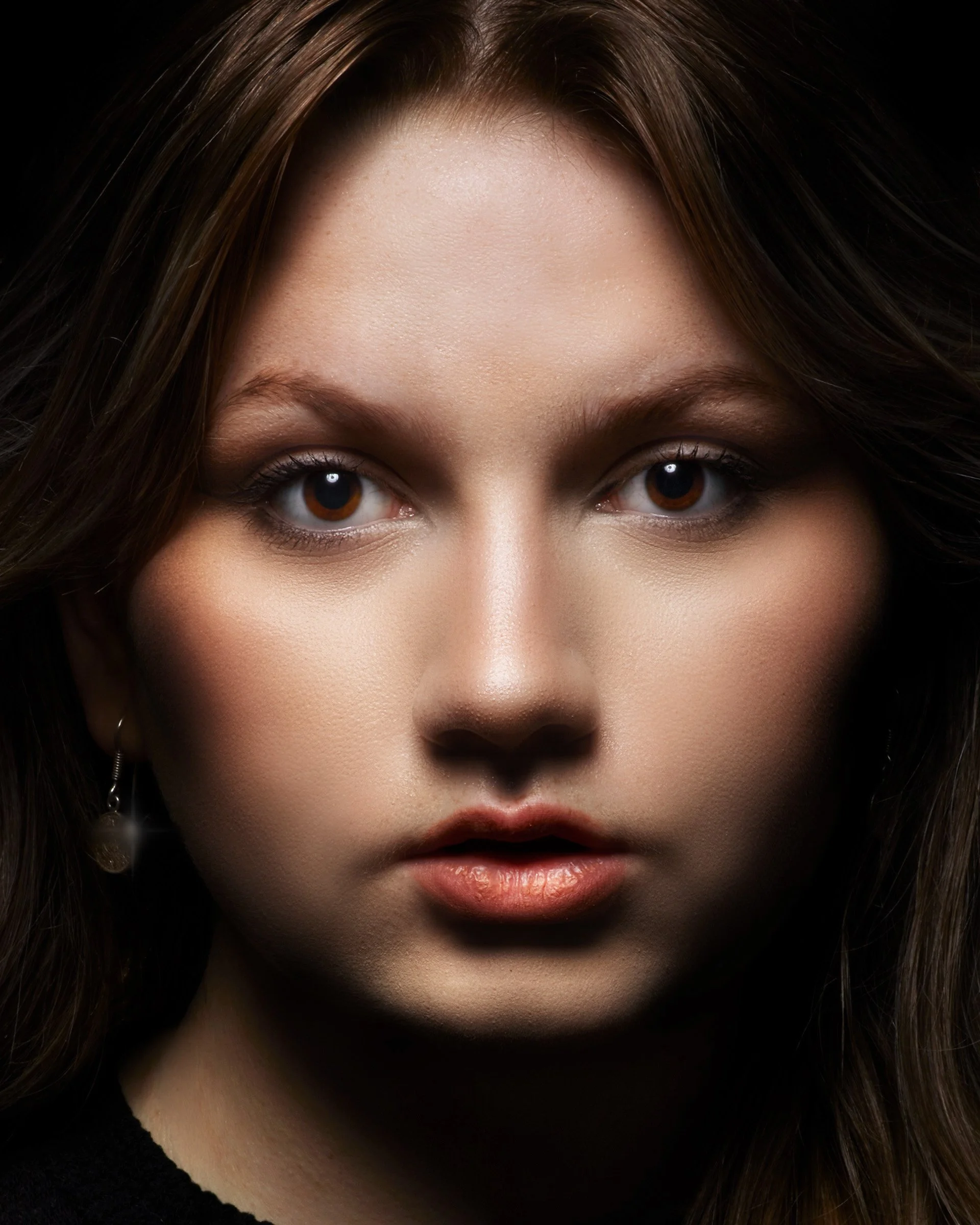 Close-up of a woman's face, focusing on her eyes, forehead, and lips with dark hair framing her face, and earrings visible on her ears.
