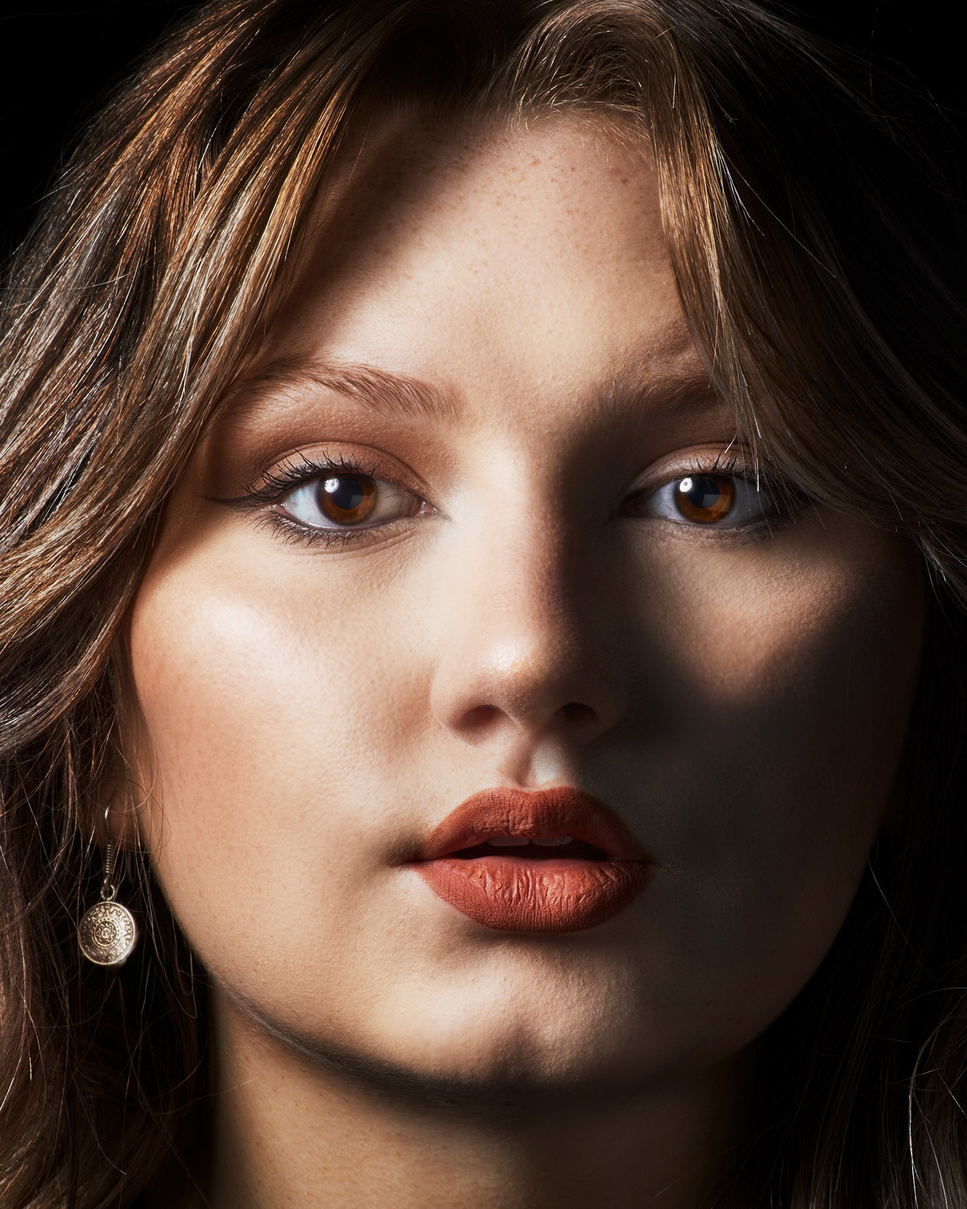 Close-up of a woman's face showing her eyes, nose, and lips with makeup, brown hair, and a dangling earring.
