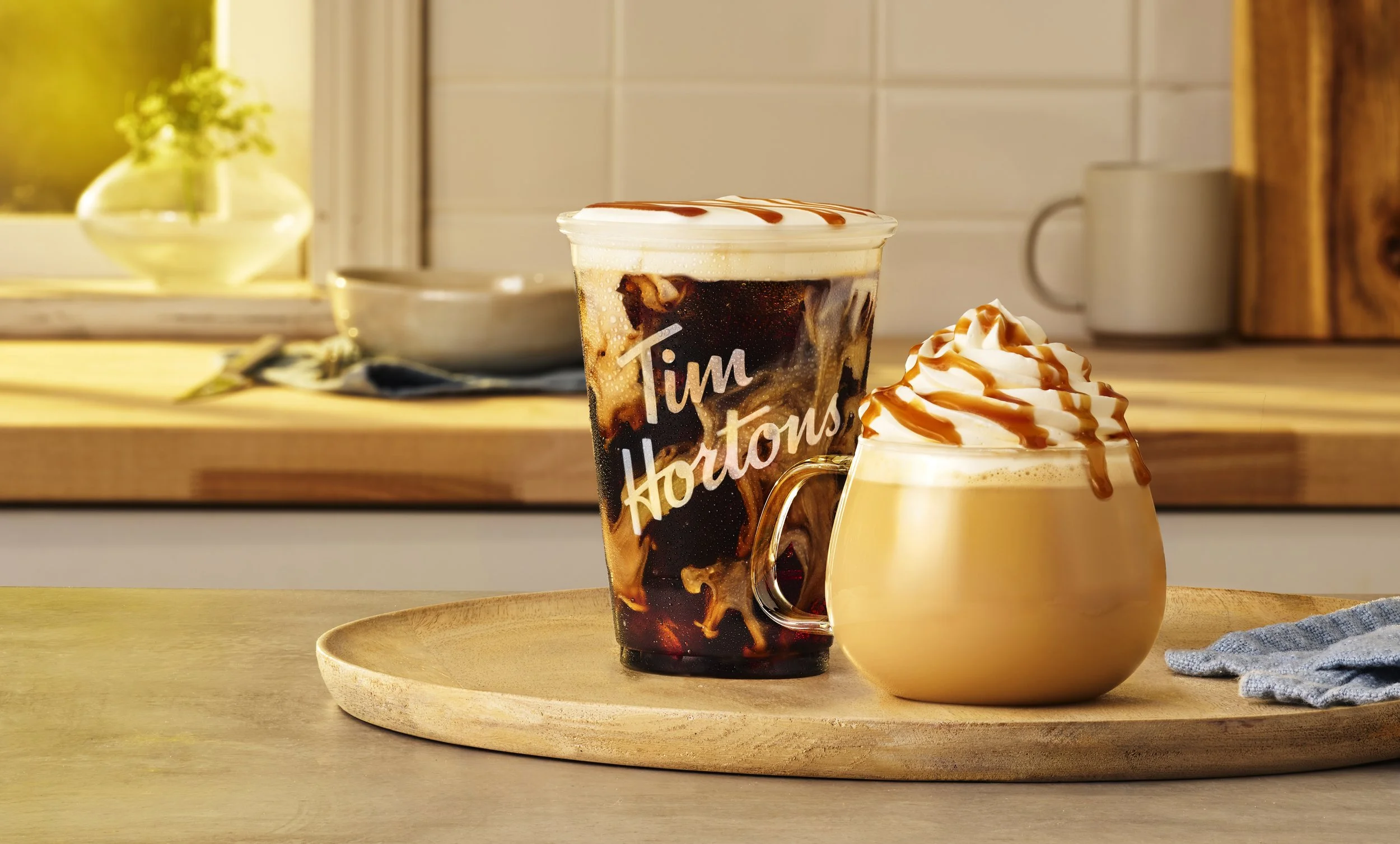 A Tim Hortons iced coffee and a caramel whipped cream topped drink on a wooden tray.