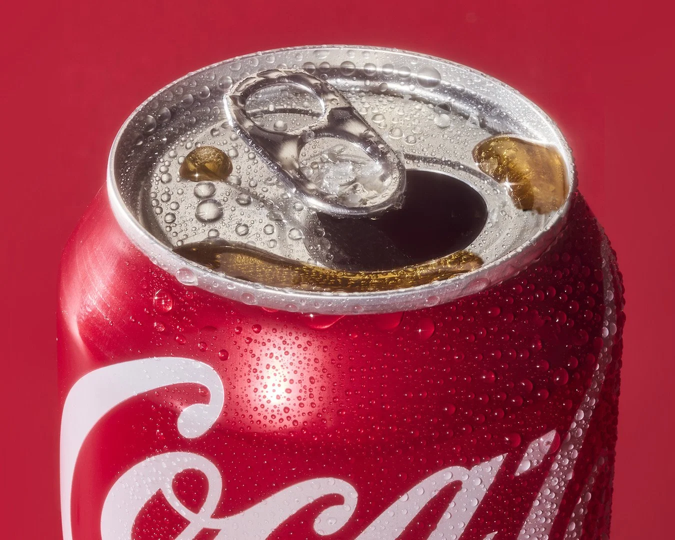 Close-up of a Coca-Cola can with condensation droplets, showing the top opening with ice cubes inside and effervescent bubbles.