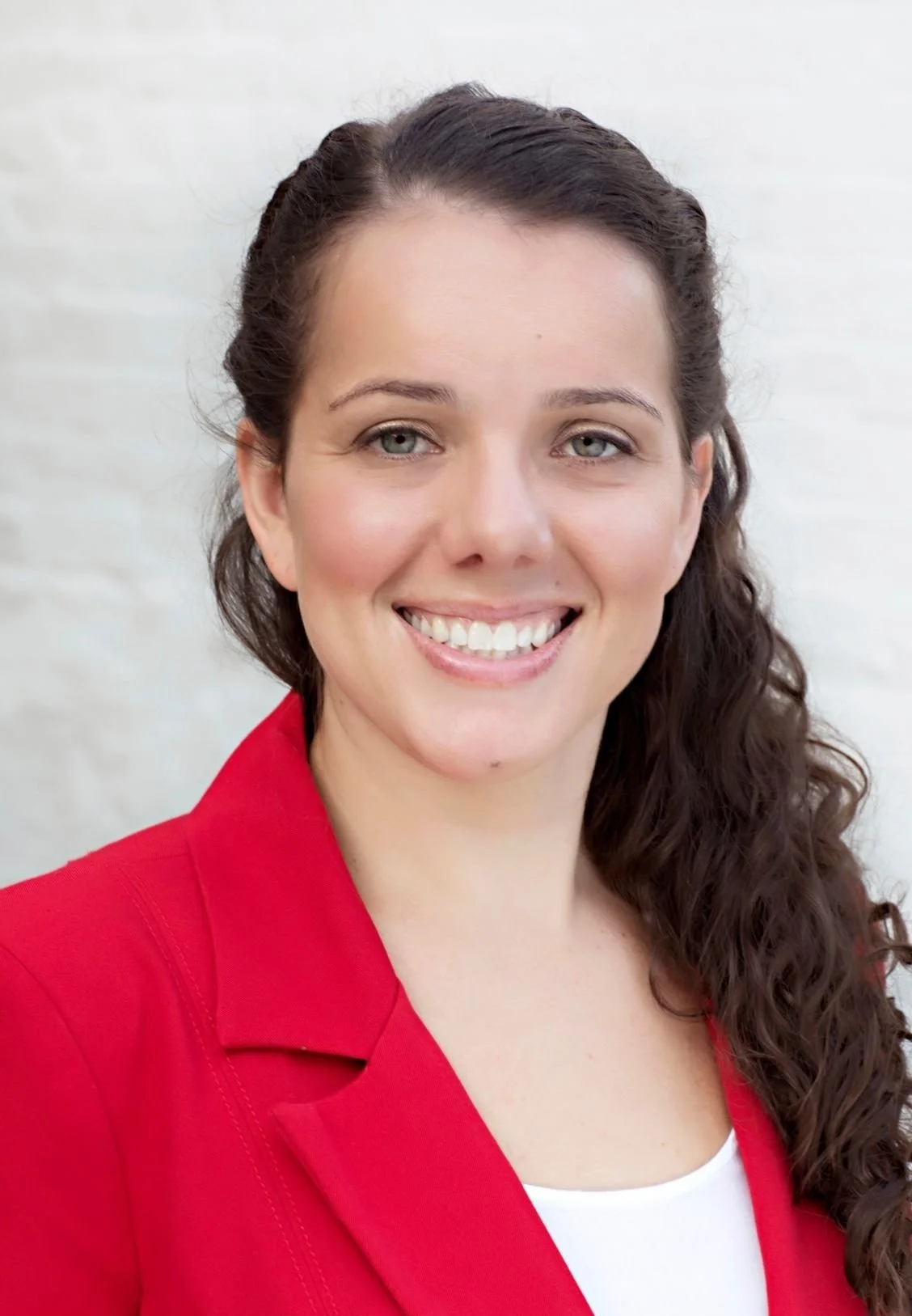 Ashley Martinez, Therapist in Lakewood, Colorado, smiling with light skin, long curly brown hair, wearing a red blazer, standing in front of a plain white background.