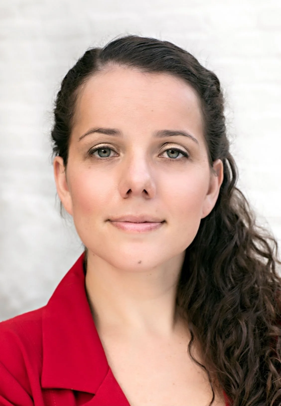 Ashley Martinez, Therapist in Lakewood, Colorado, with dark brown wavy hair, blue eyes, and light skin, wearing a red top, smiling gently at the camera with a blurred light background.