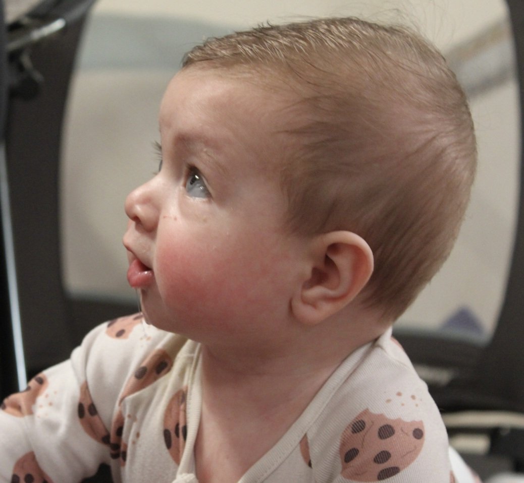 A young child with light brown hair and blue eyes looking to the side, wearing a white shirt with a brown and black polka dot pattern.