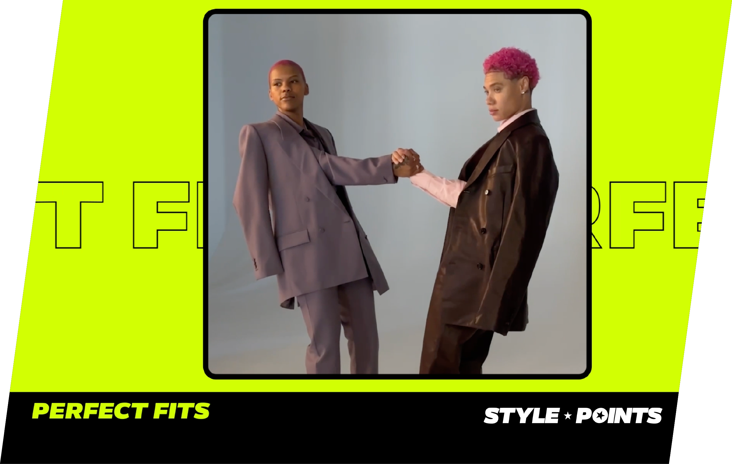 Two individuals with short hair shaking hands in a studio with a plain light gray background. The person on the left has pink hair and is wearing a gray suit. The person on the right has curly pink hair and is wearing a brown leather jacket over a pink shirt.