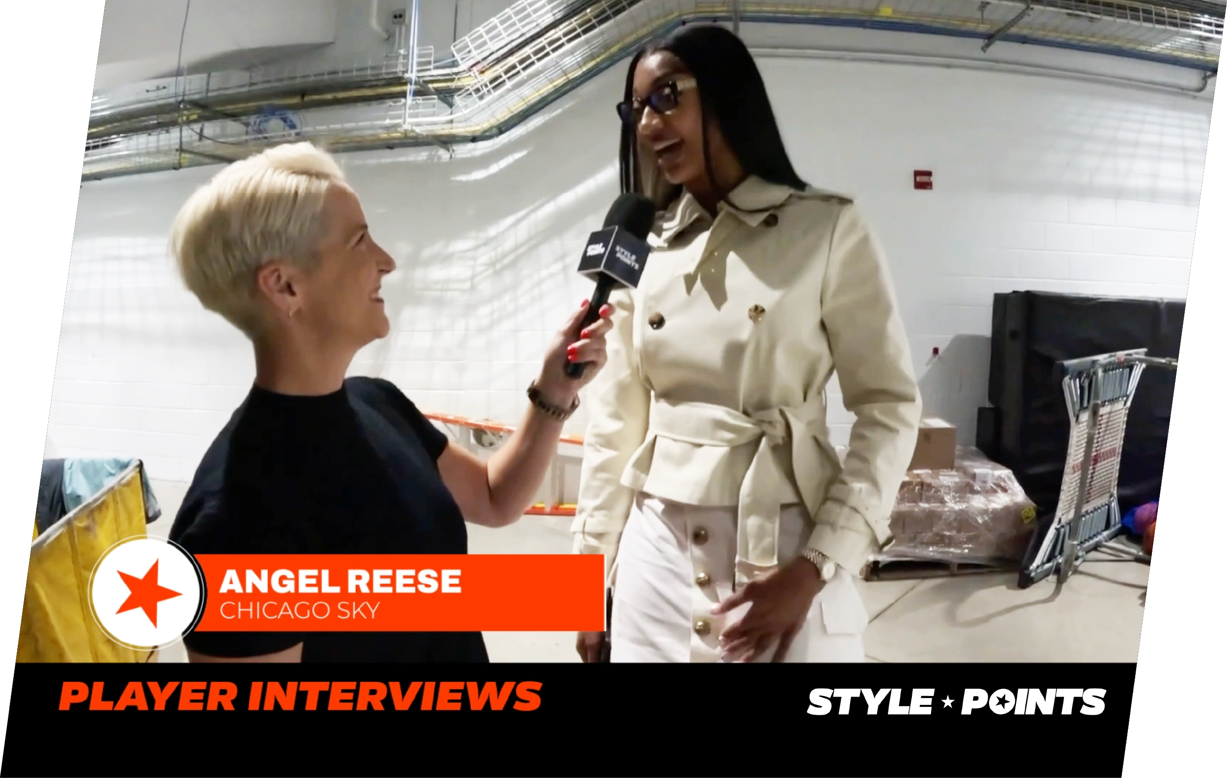 A woman in glasses and a cream-colored coat is being interviewed by another woman with short platinum blonde hair, in an indoor setting. The interviewee is smiling and wearing a gold bracelet, with various industrial pipes and equipment in the background. A lower third graphic displays her name Angel Reese from Chicago Sky, with a section for player interviews.