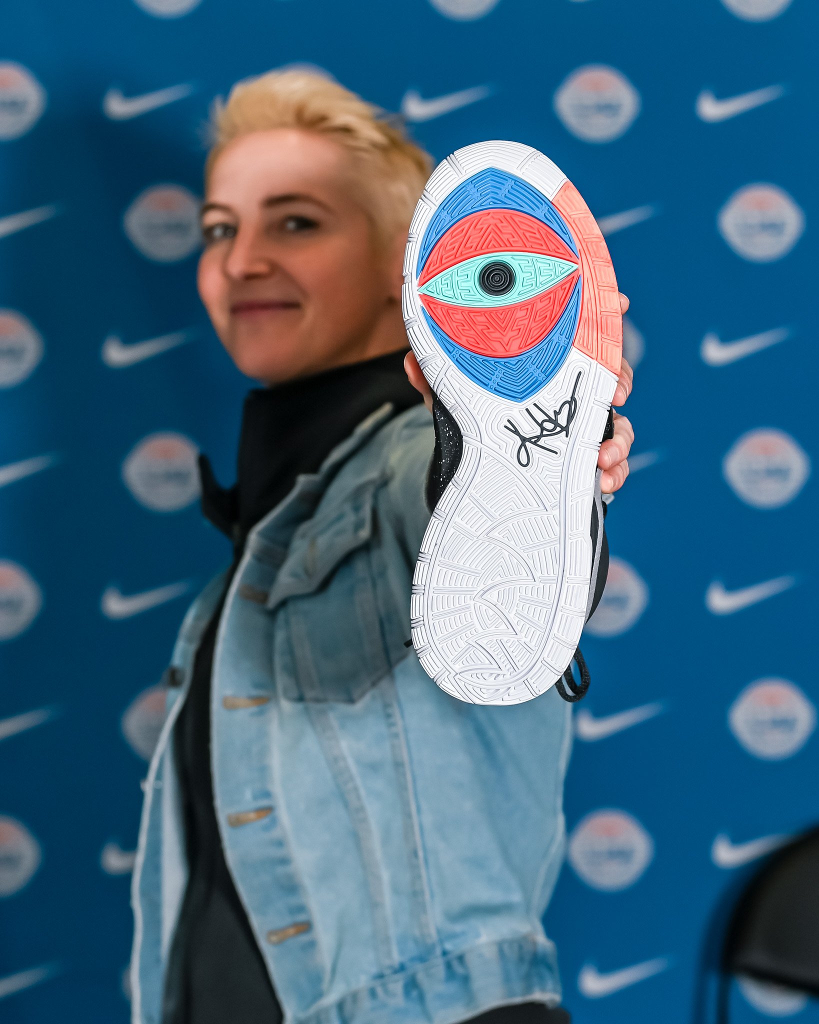 A person holding a colorful sneaker with a detailed sole in front of a blue backdrop with Nike and NBA logos.