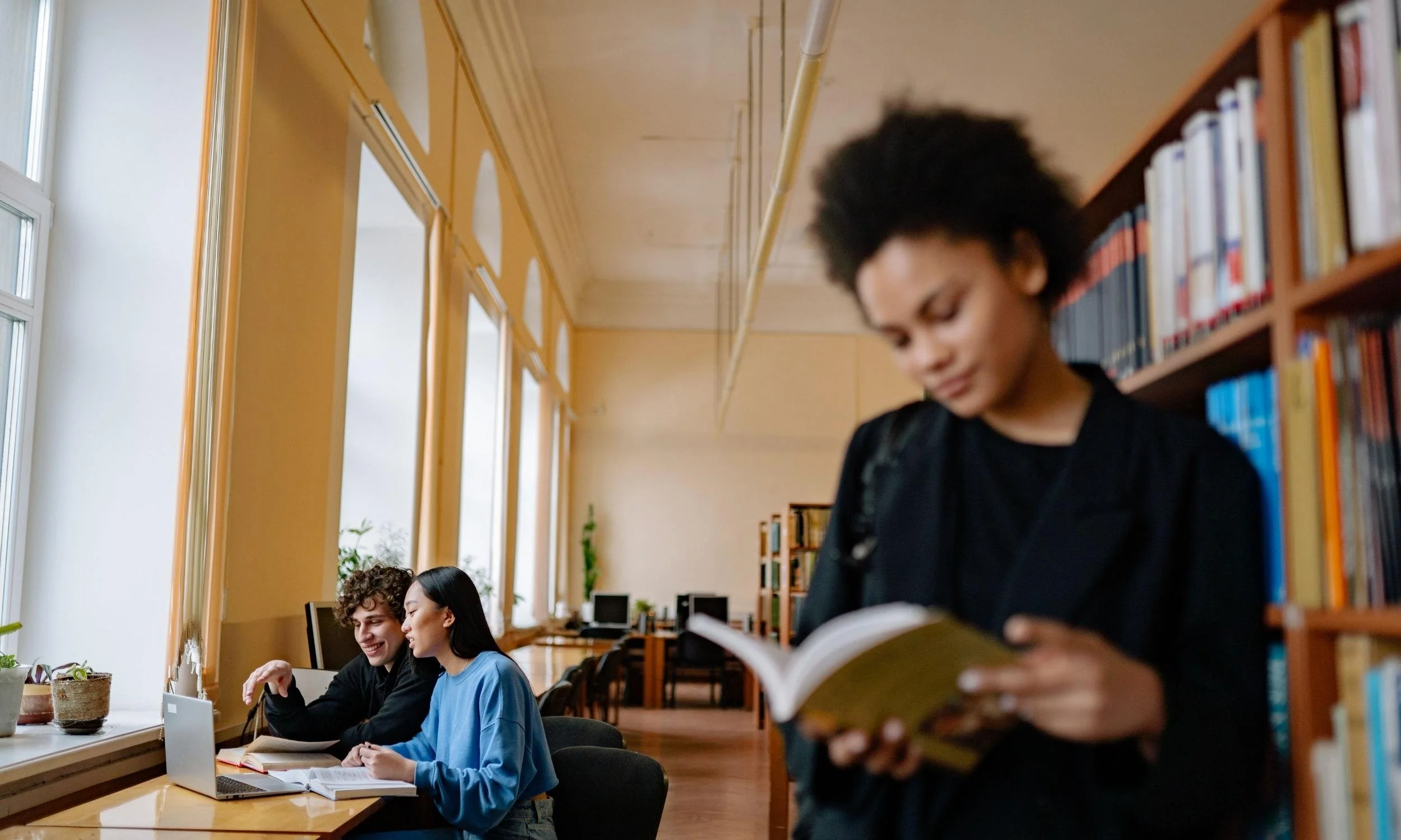 Student reading in a library while others collaborate. The Cottage Hill Excellence Foundation, a 501(c)(3) nonprofit organization supports academic achievement and leadership.