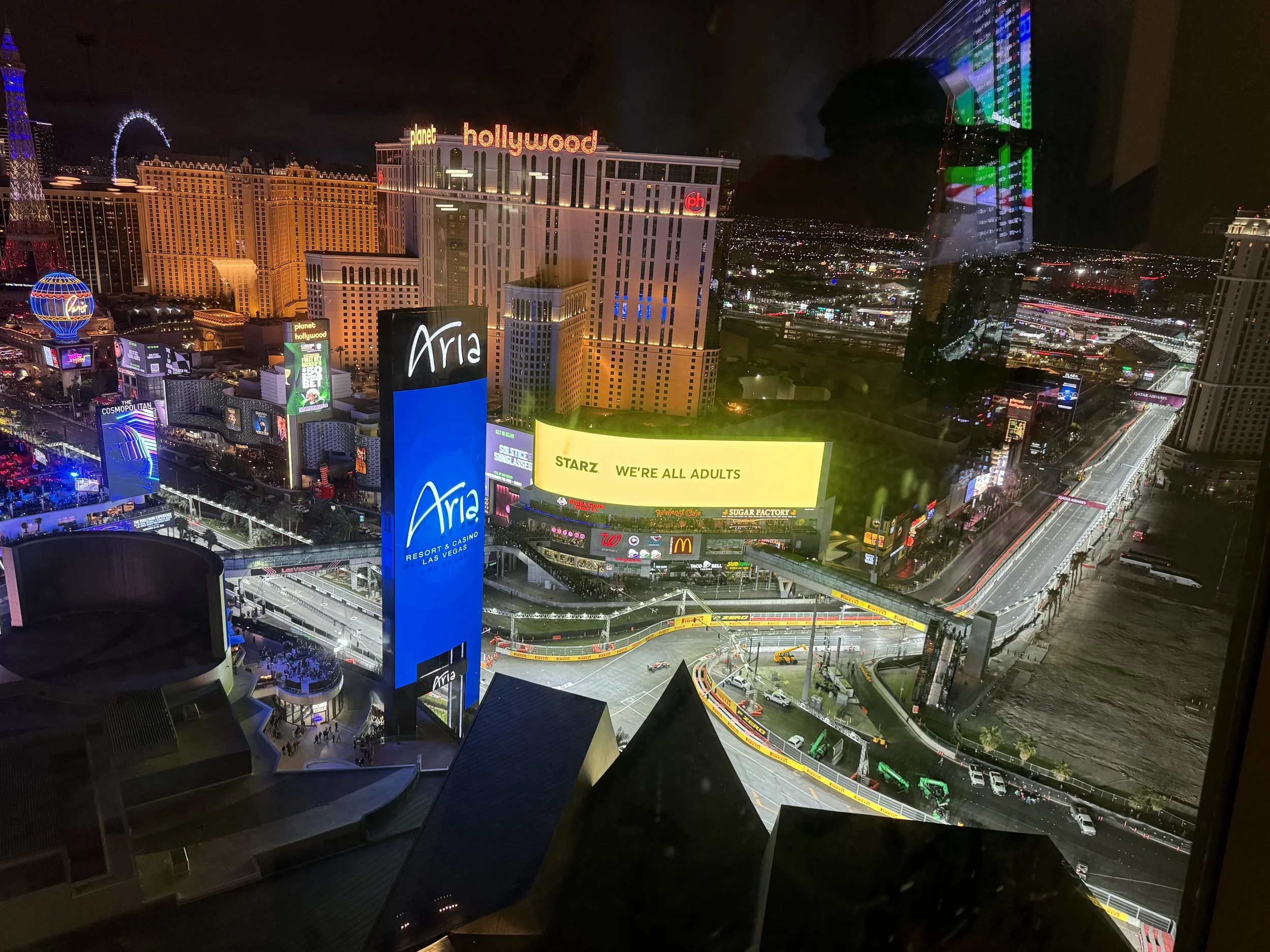 Nighttime cityscape of Las Vegas during Formula One from a private viewing party with illuminated signs and buildings, including the Aria Resort and Casino, Las Vegas Strip, and surrounding structures, viewed from a high vantage point.