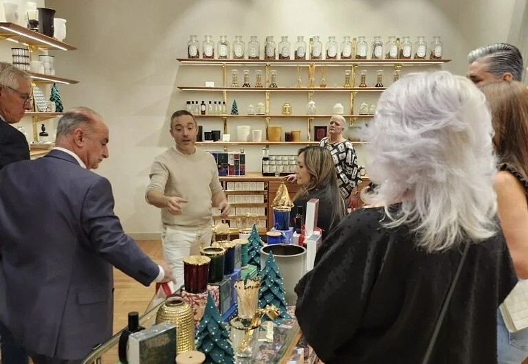 People gathered around a display table with holiday-themed decorations, in a store or gallery setting with shelves filled with glass jars and decorative items in the background for a Masterclass.