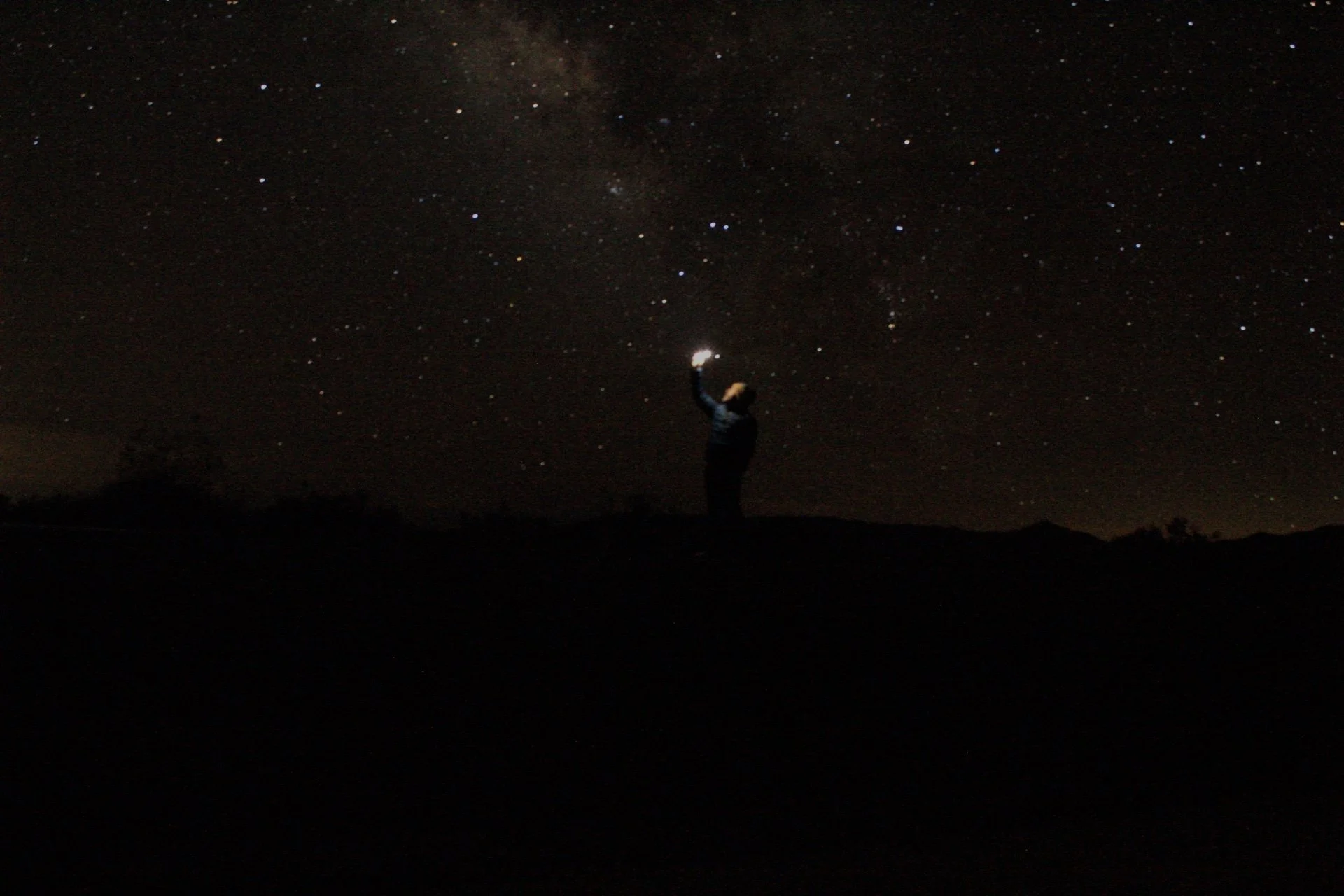 A person holding a light beneath the Milky Way in the desert outside Las Vegas.