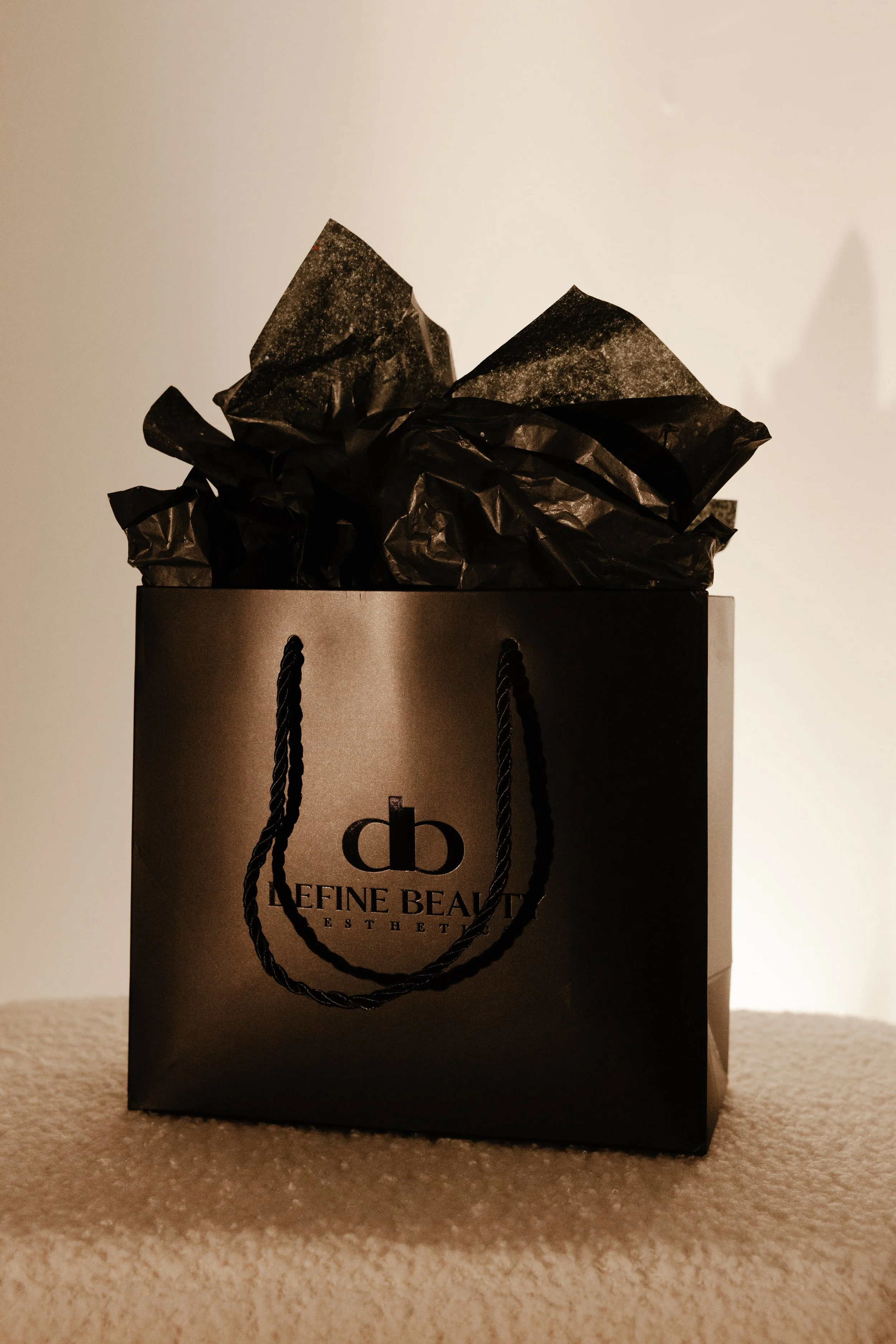 A black shopping bag from LaFeine Beauty, with black tissue paper inside, resting on a beige carpet.