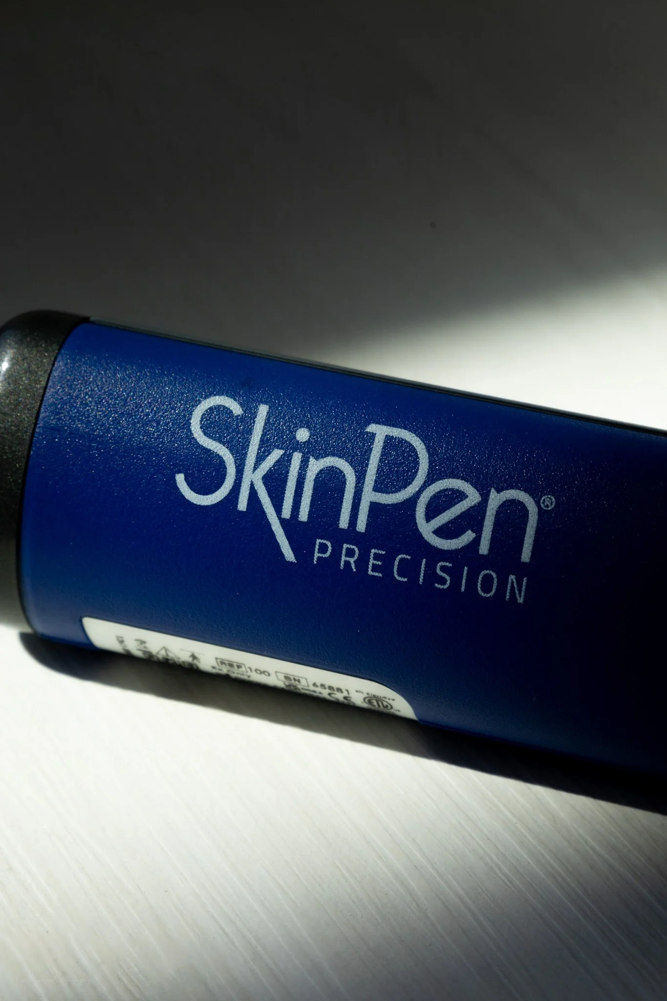 A blue tube of SkinPen Precision skincare product lying on a white surface with part of the label visible.