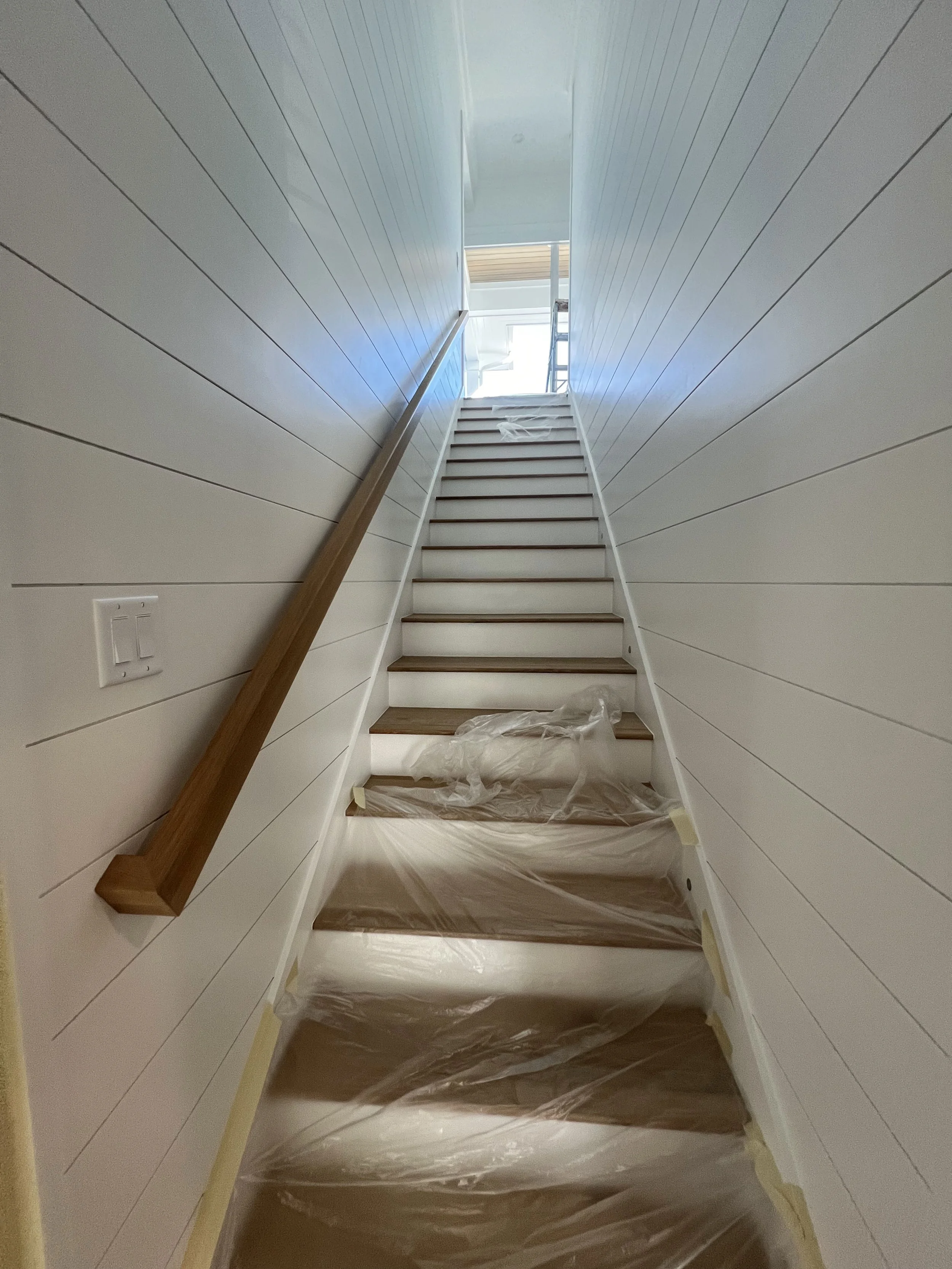 Staircase with a wood handrail and white horizontal wall paneling — Project 05.