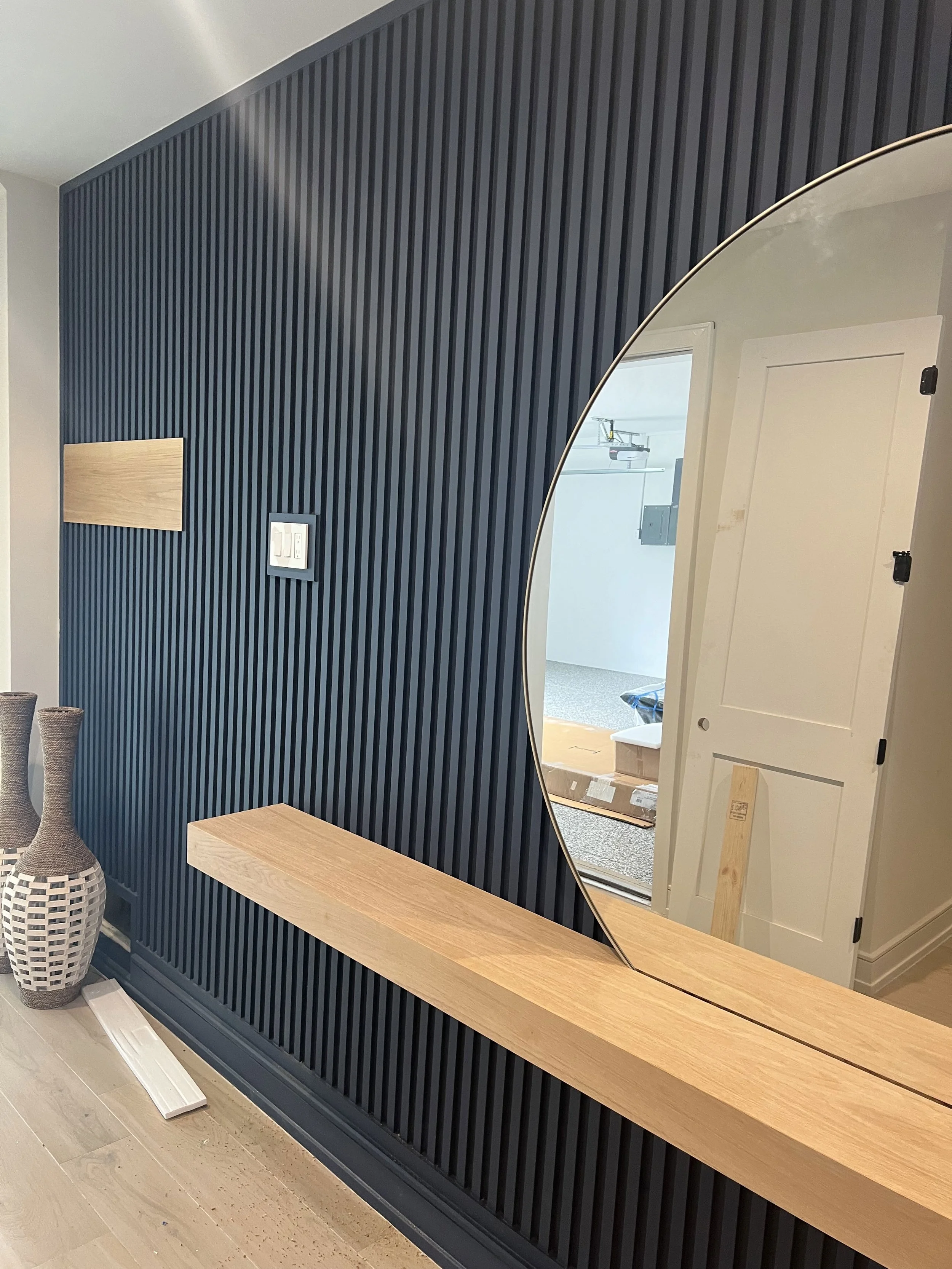 Round mirror and wood vanity shelf against a blue paneled wall — Project 02.
