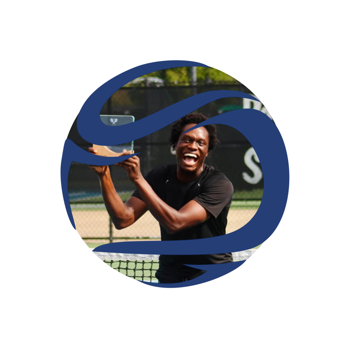 A man with curly hair and a black T-shirt holding a tennis trophy and smiling in front of a tennis court.