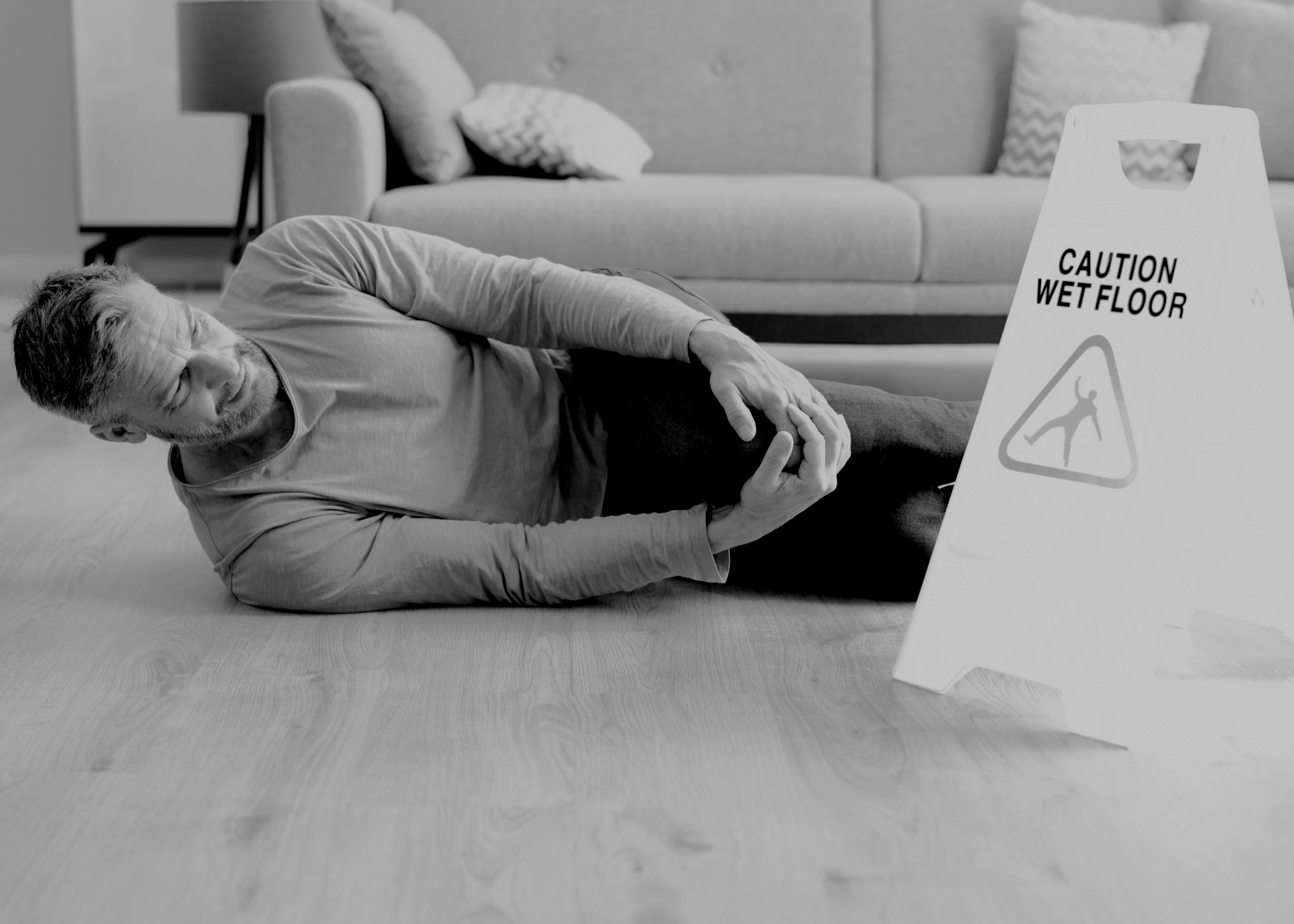 An older man lies on the floor, about to fall, near a wet floor sign that reads 'Caution Wet Floor' with a warning symbol.