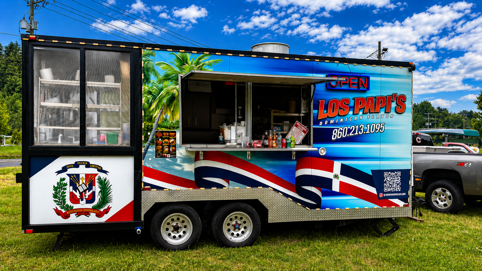 A vibrant food truck with Dominican Republic and American patriotic theme, featuring an open window menu with condiments, an 'OPEN' sign, and phone number, parked on grassy area with trees and blue sky in the background.