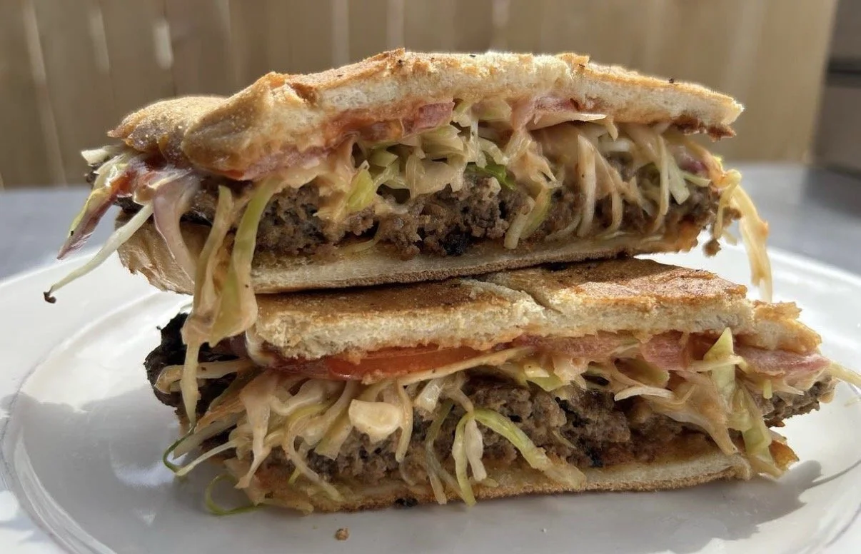 A double-layer toasted sandwich with ground beef, shredded lettuce, tomato slices, cheese, and sauce on white bread, served on a white plate.