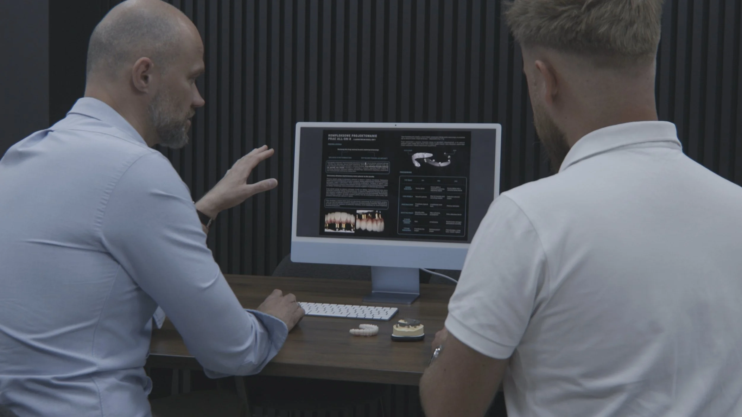 Two men in white shirts sitting at a desk, discussing dental treatment options displayed on a computer screen.