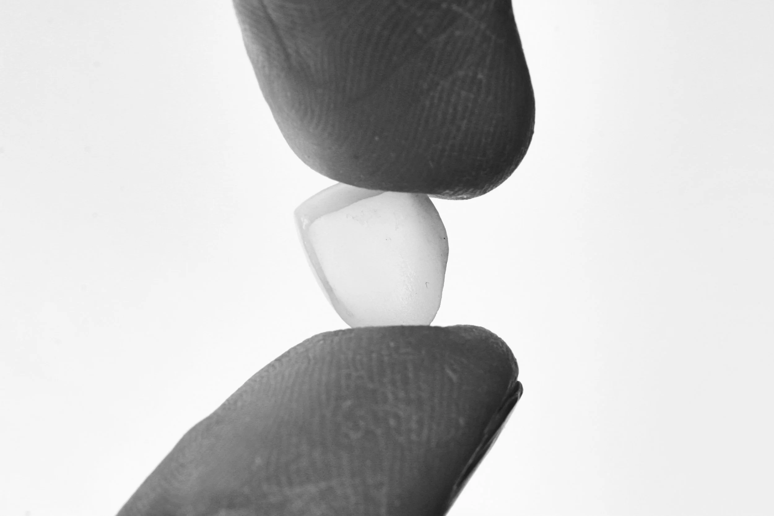 Close-up of fingers balancing a small white object between two fingers, with a mostly black and white background.