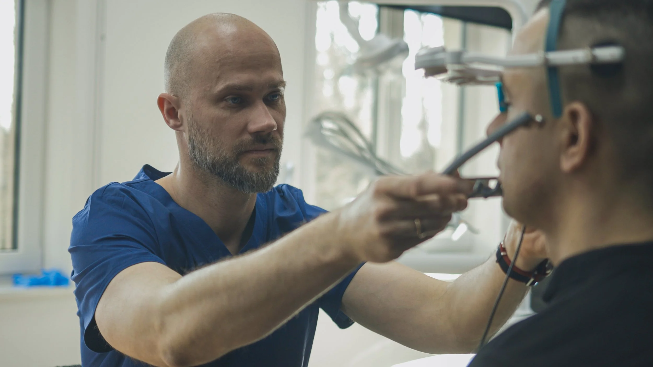 A healthcare professional in blue scrubs examines a young patient's throat with an endoscope in a clinical setting.