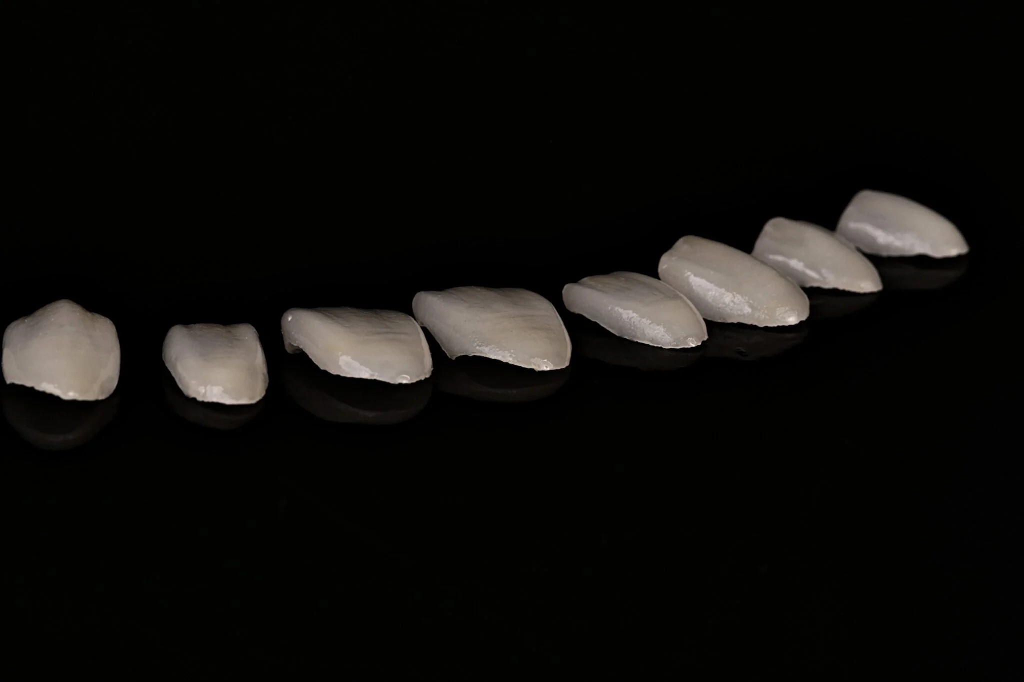 Row of partially peeled garlic cloves on a black reflective surface.