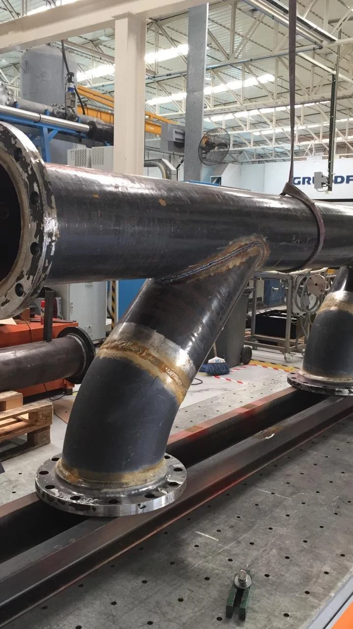 Probeta grande de metal con tubería conectada en un entorno industrial, posiblemente una fábrica o planta de manufactura.