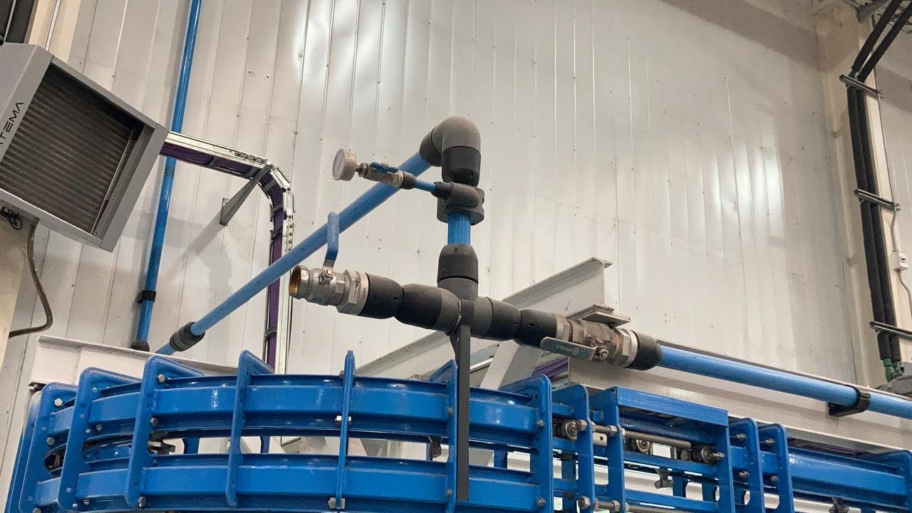 Sistema de tuberías y maquinaria en un entorno industrial con estructura metálica y paredes de paneles blancos.