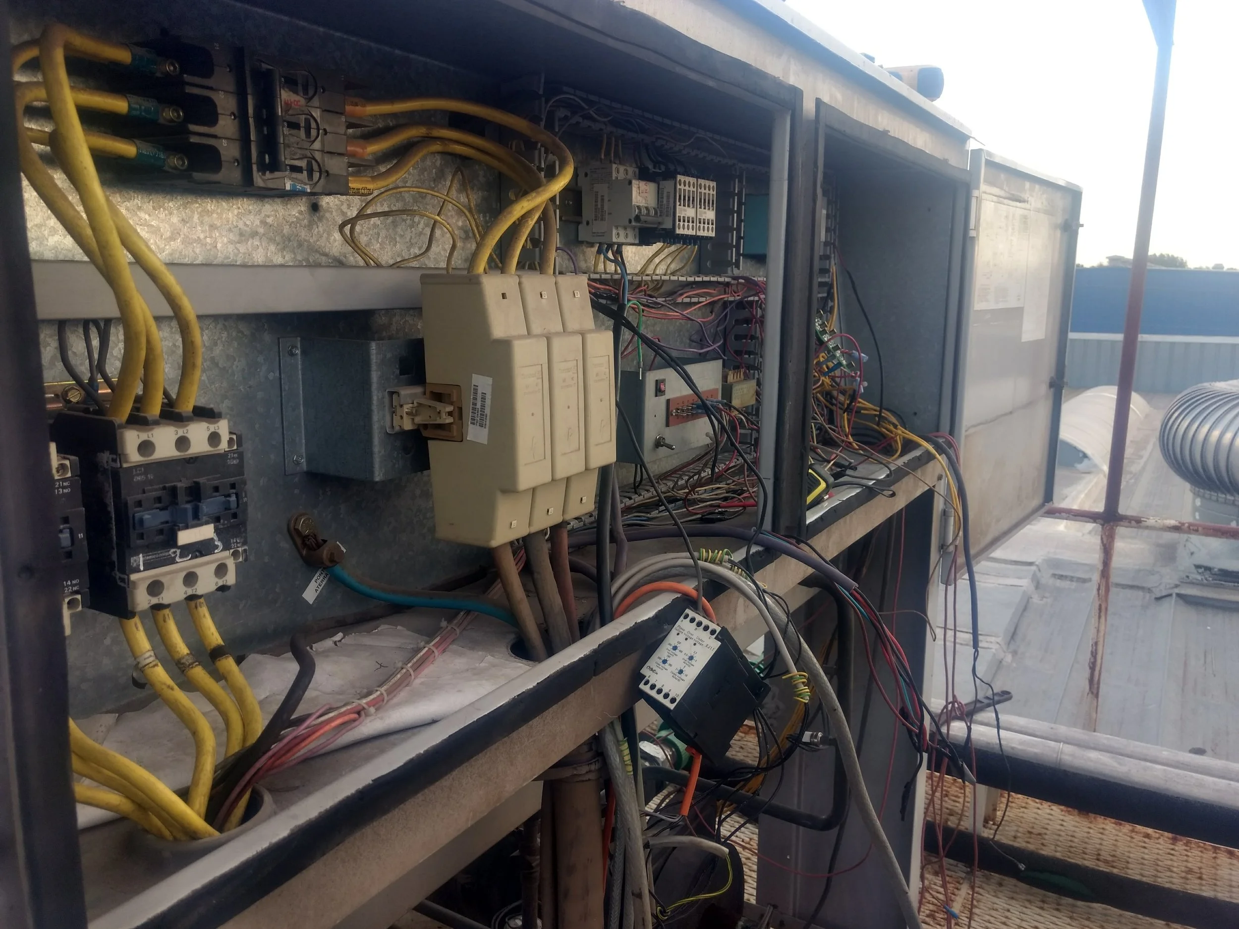 Panel de control eléctrico con cables y componentes electrónicos en una estructura de metal, en un lugar al aire libre.