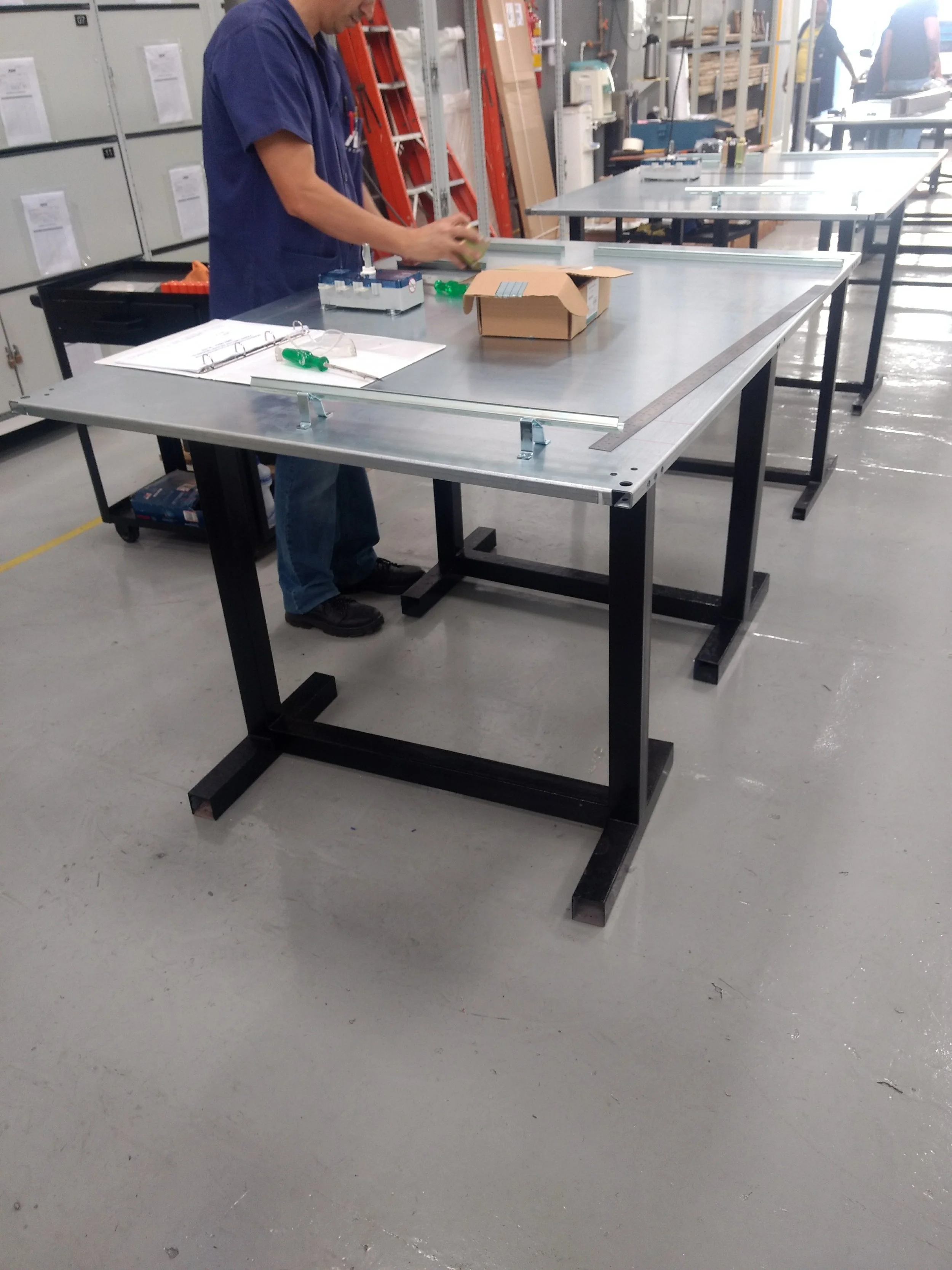 Persona trabajando en un taller de carpintería, ensamblando madera sobre una mesa de trabajo metálica.