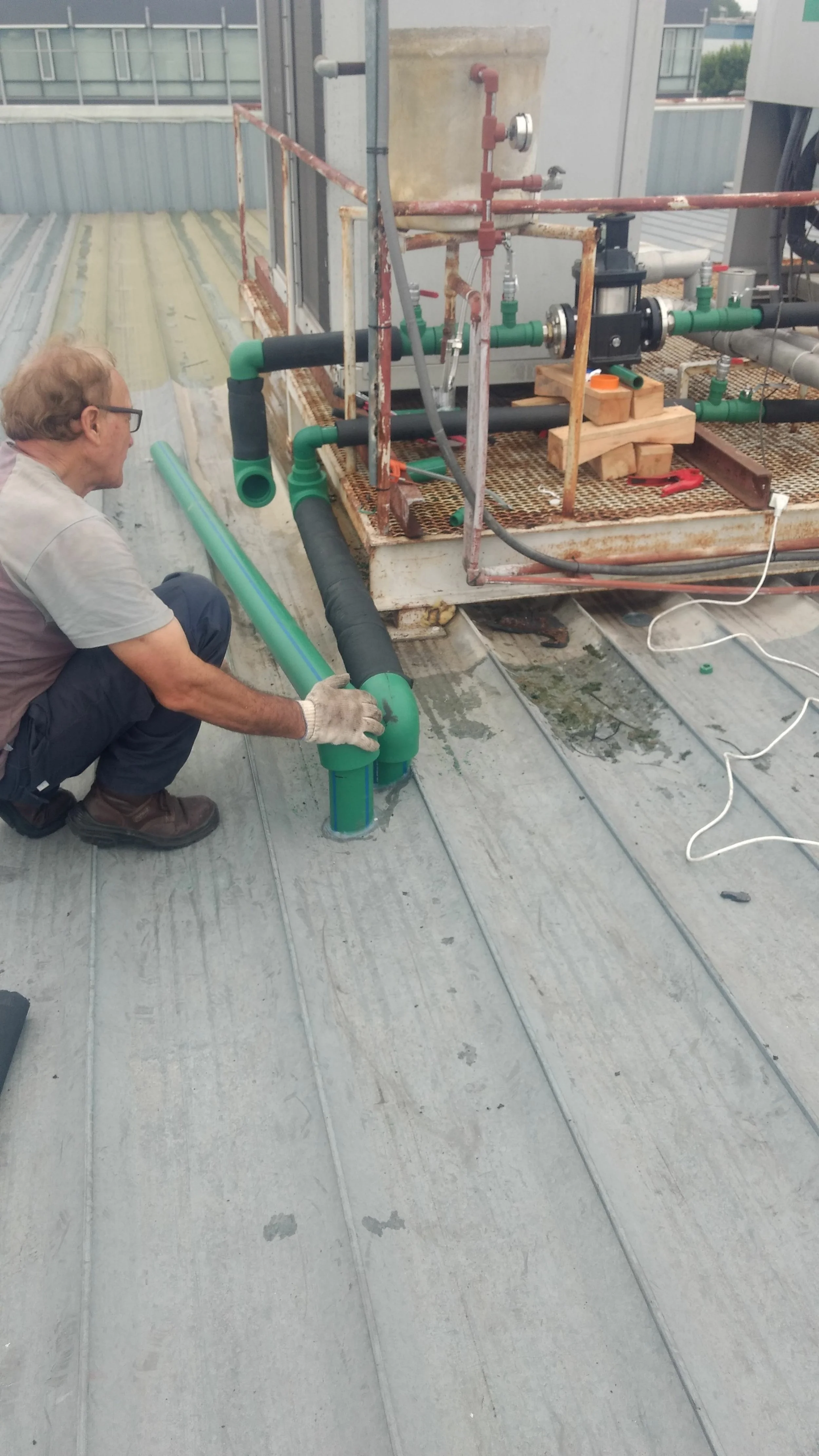 Un técnico instala tuberías de PVC en una azotea para un sistema de plomería o aire acondicionado, con herramientas y un sistema de control en la escena.
