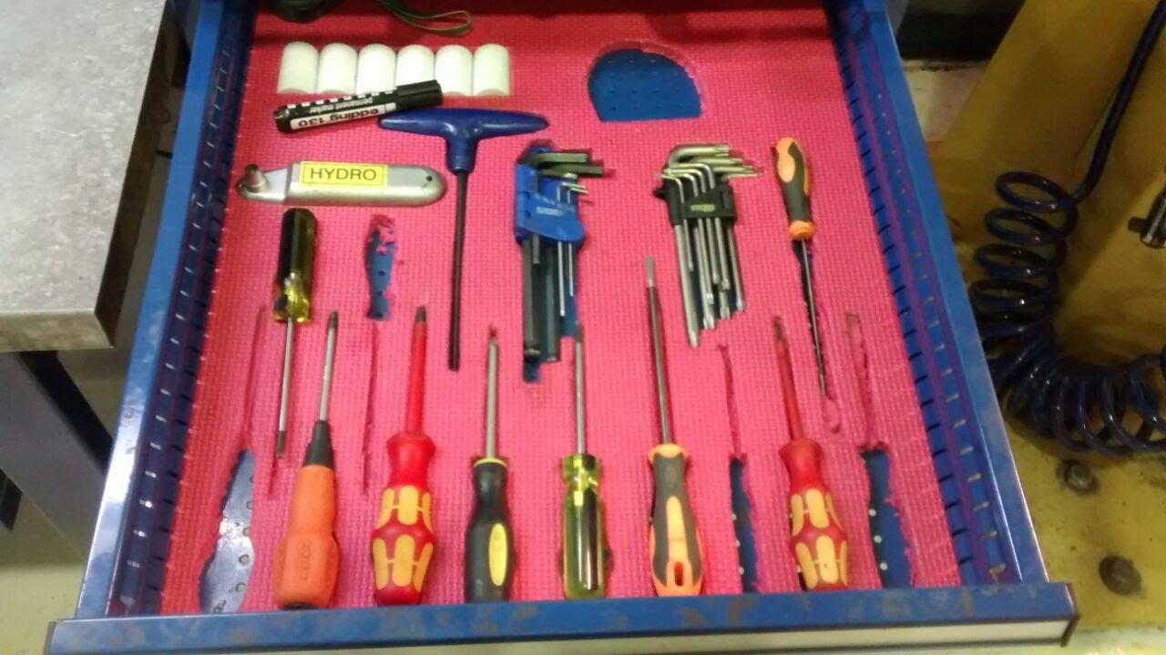 Caja de herramientas con destornilladores, llaves, brochas y otros instrumentos, todo ordenado en un tapete rojo.