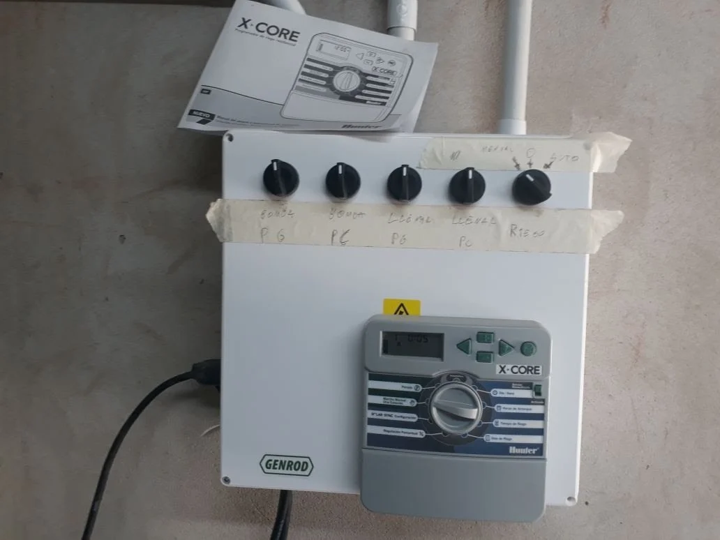 Cuadro eléctrico de control de un sistema de rociadores automáticos, con cuatro perillas y un temporizador digital.